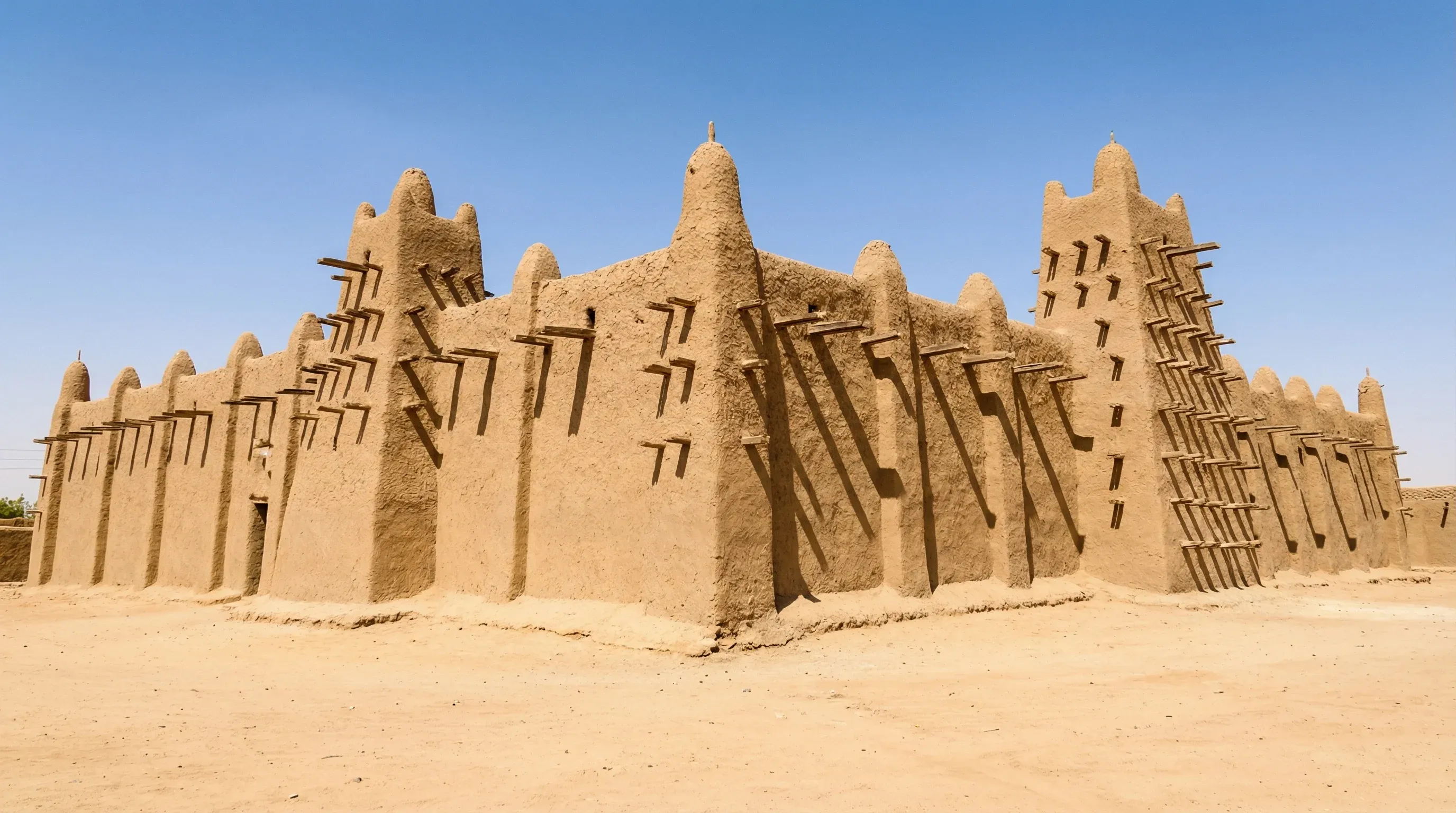 The historic Djinguereber Mosque in Timbuktu, Mali, showing its unique earth-and-timber construction under a bright sun.