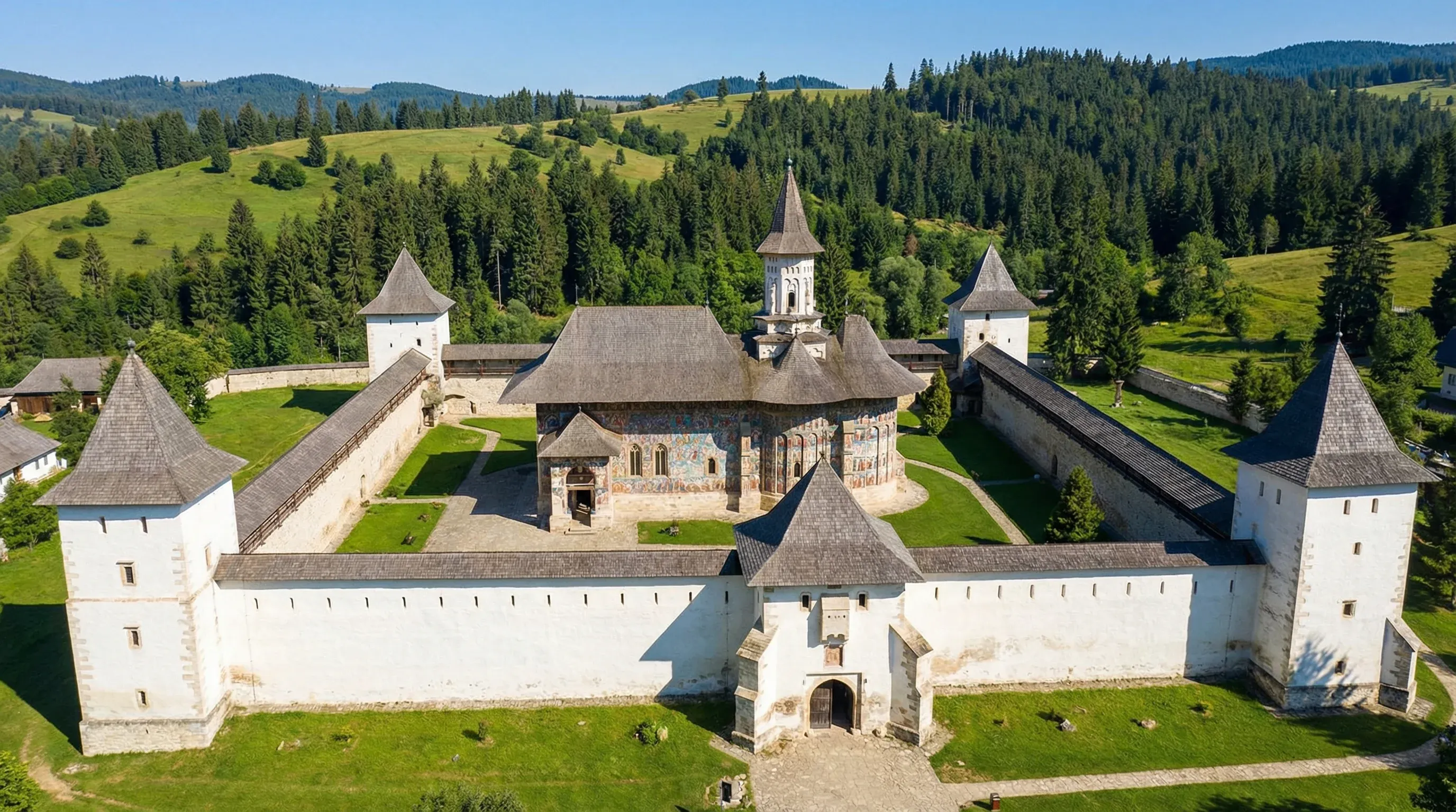 A high-angle view of the fortified Sucevița Monastery church with painted exterior walls in a green valley.