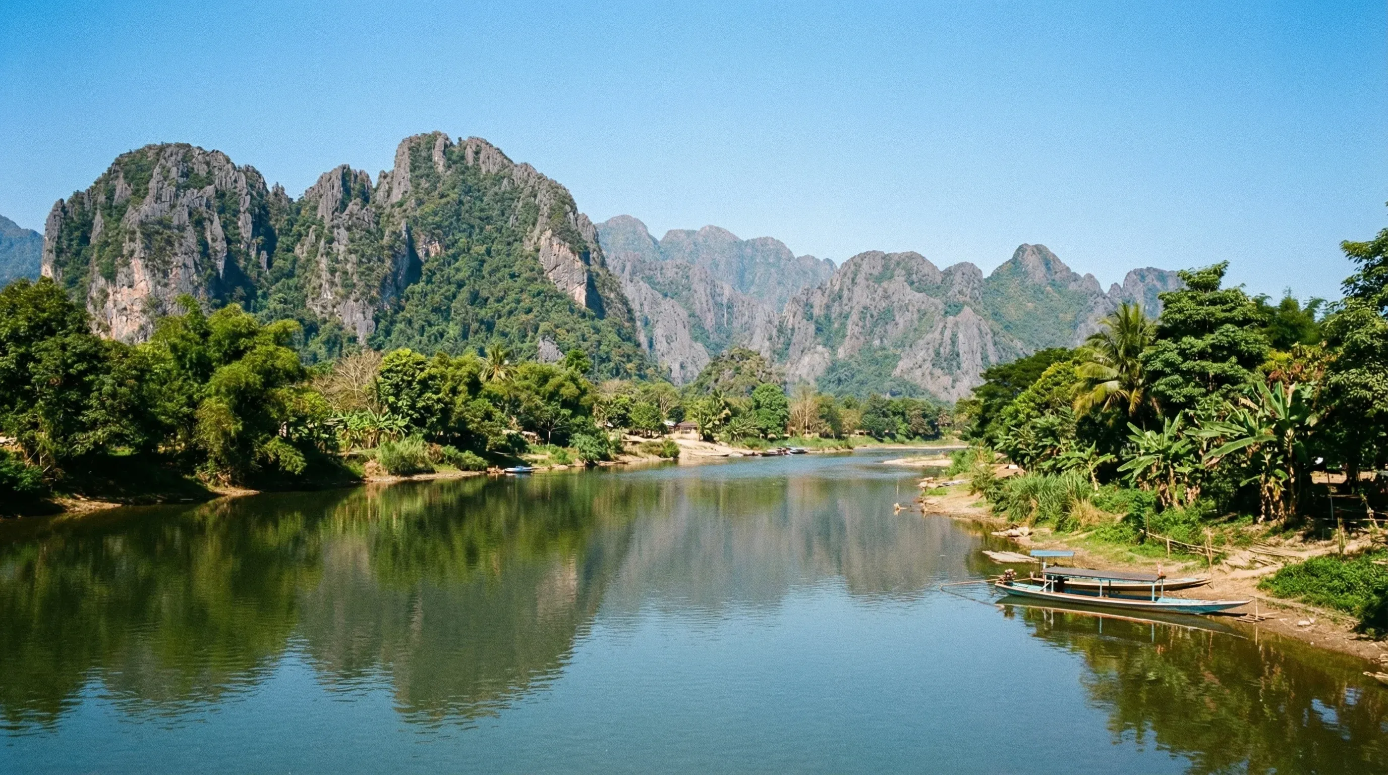 The Nam Song River in Vang Vieng with a backdrop of tall, jagged limestone karst mountains.