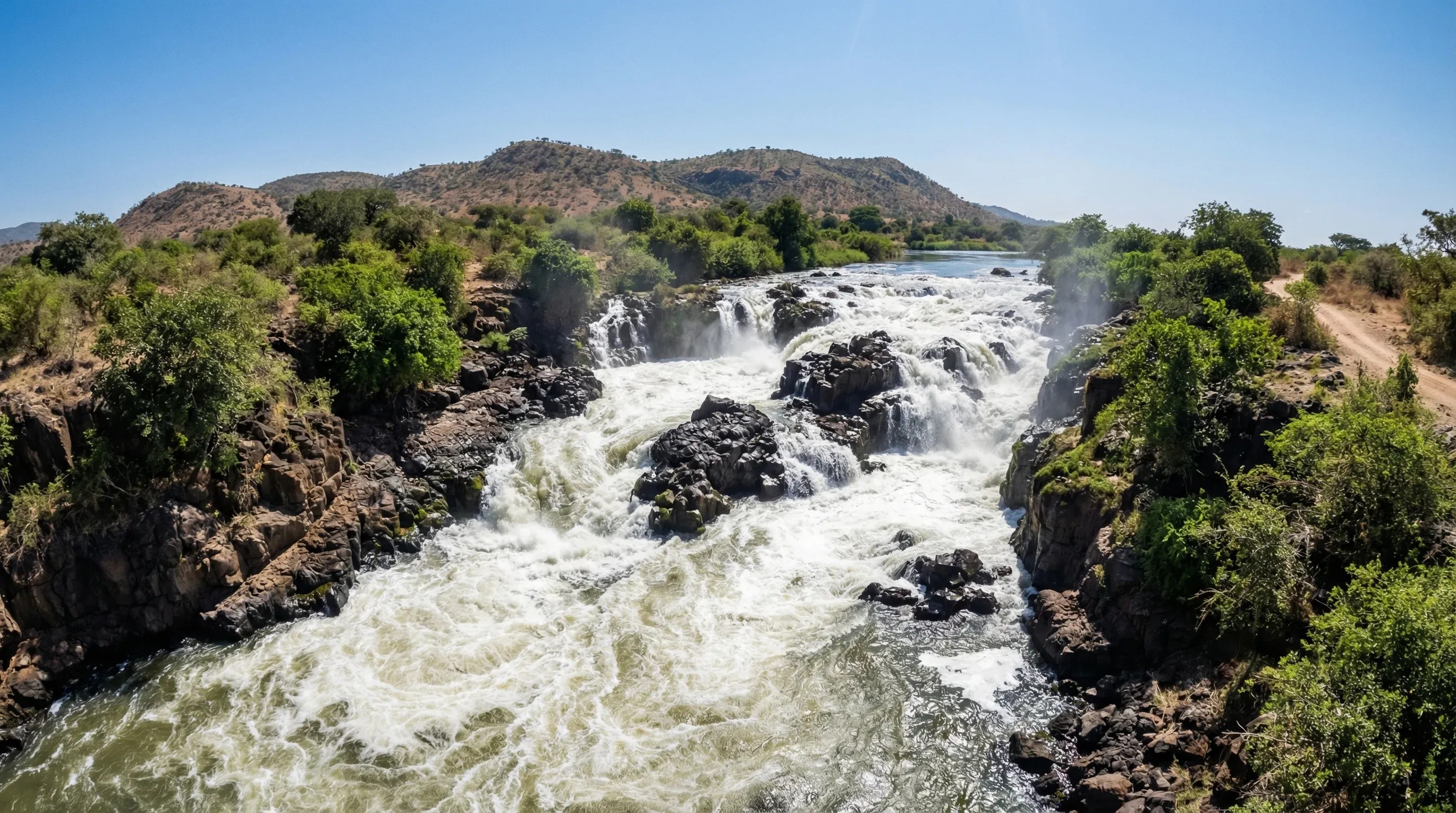 A view of the white water rapids of the Nile at Fola Rapids in Nimule National Park, with rocky banks and green vegetation.