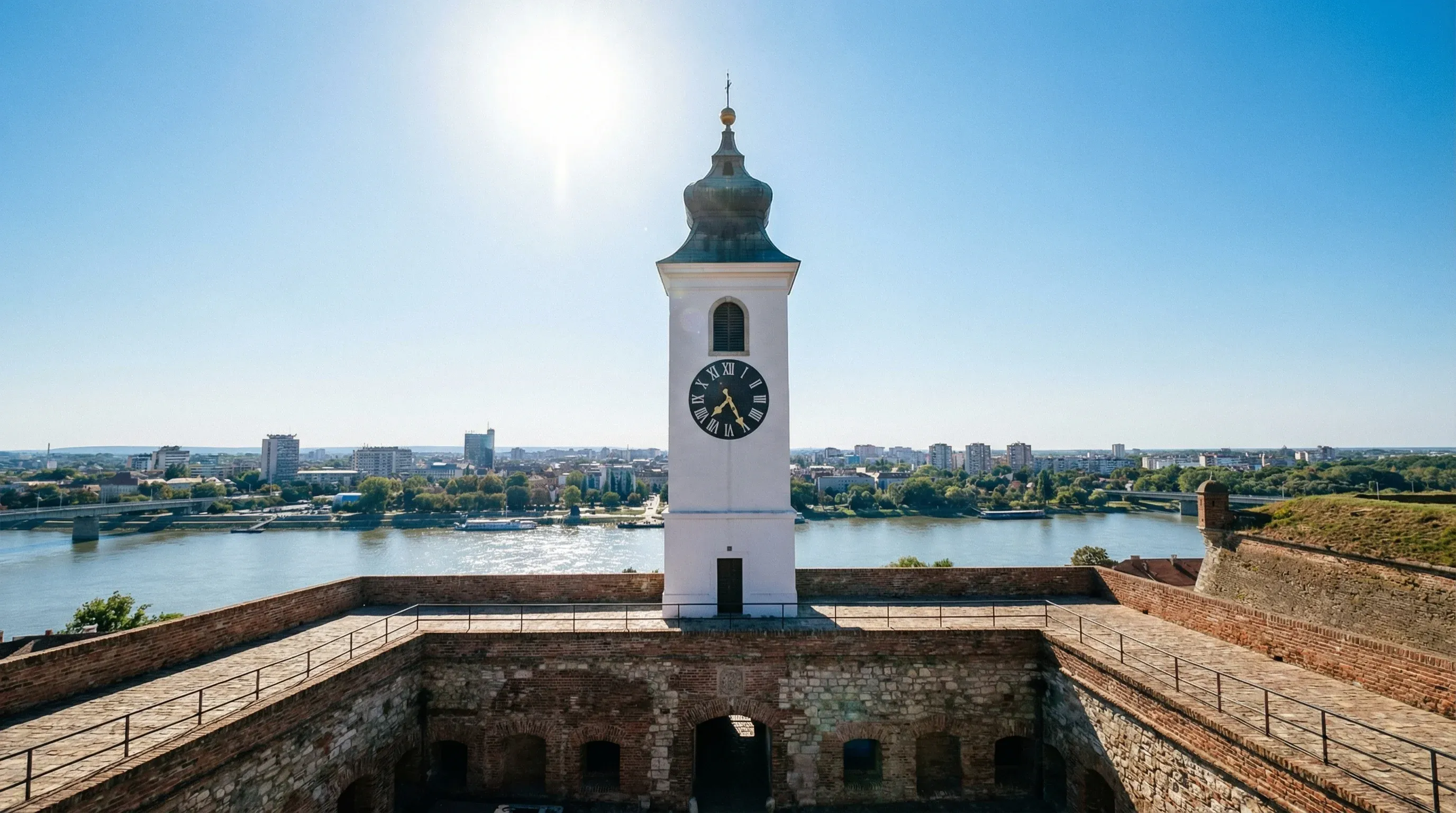 The historic white clock tower of Petrovaradin Fortress overlooking the Danube River and the city of Novi Sad.