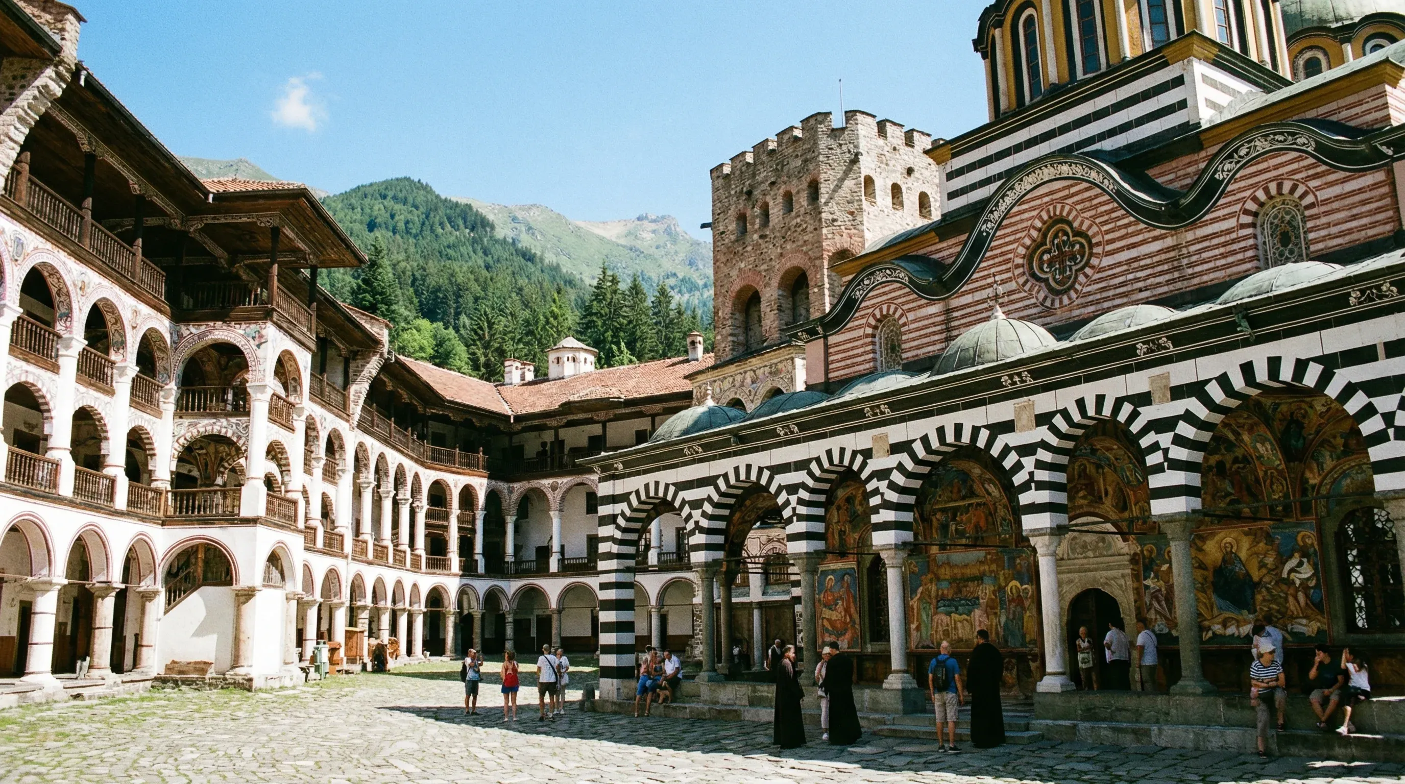The inner courtyard of Rila Monastery in Bulgaria, displaying traditional striped archways and frescoes against the Rila Mountains.
