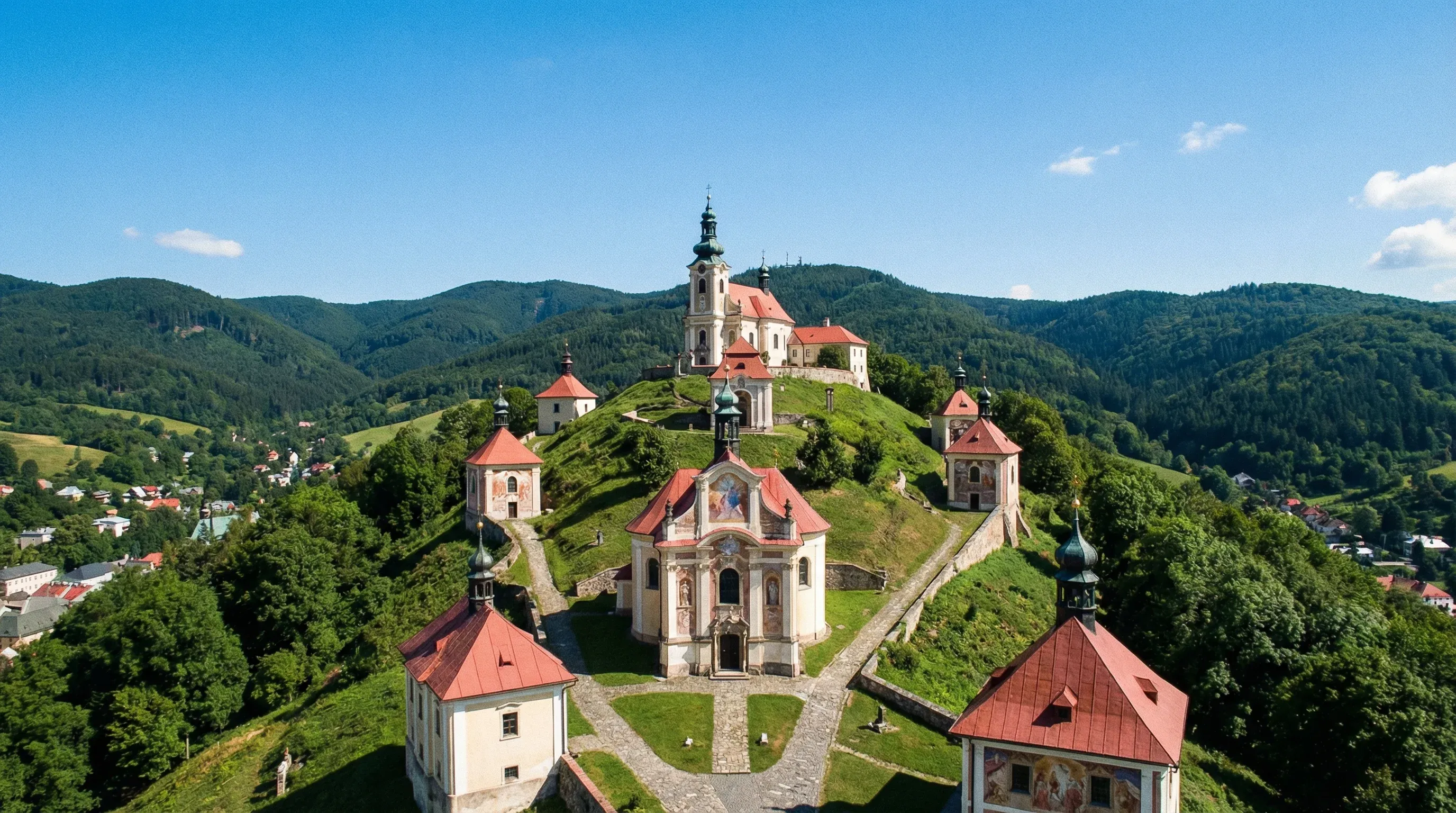Historical baroque chapels and churches built onto the side of a grassy hill in Central Slovakia.