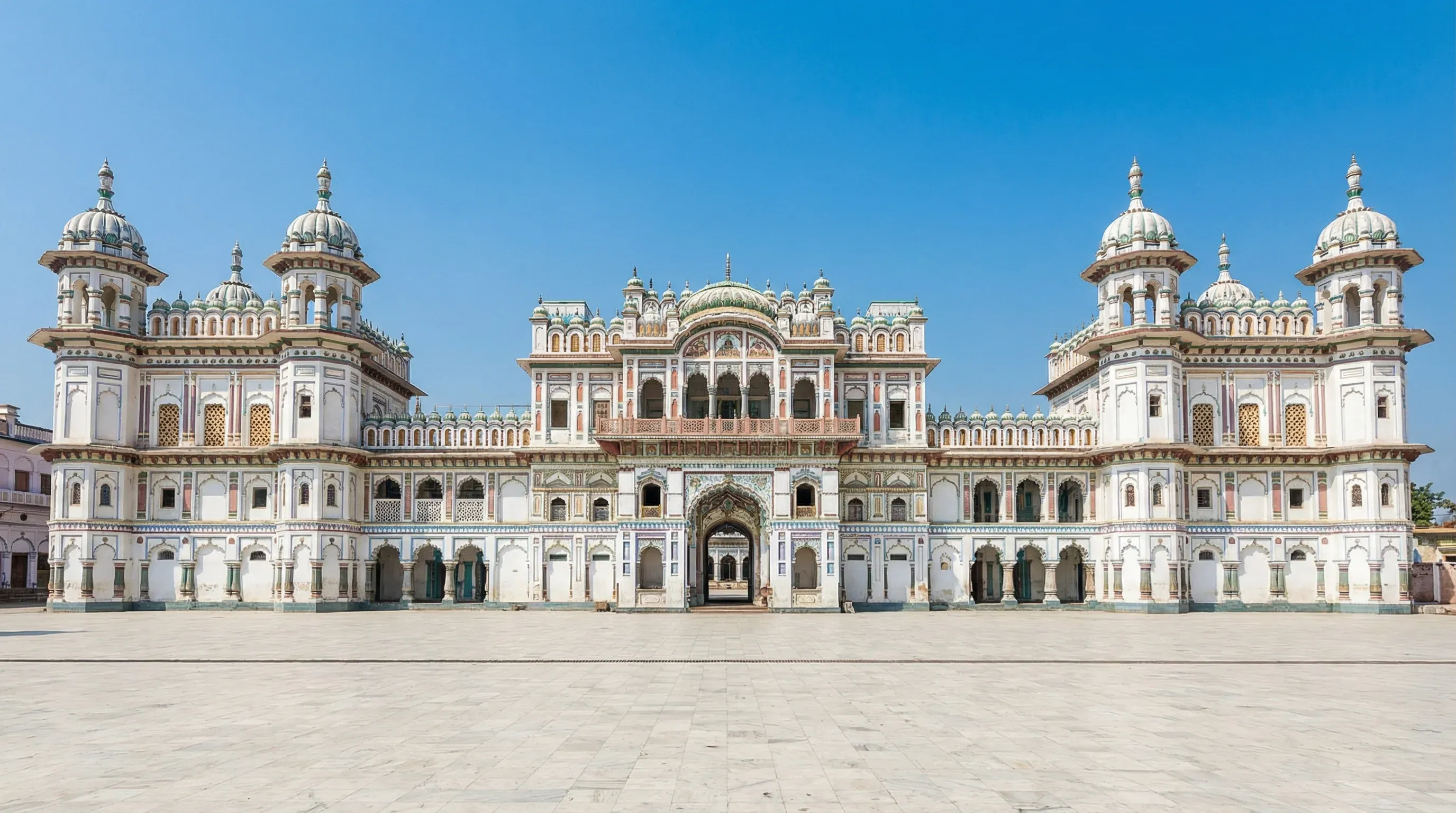 The Janaki Mandir temple in Janakpur, showing its white and pastel multi-domed architecture against a clear blue sky.