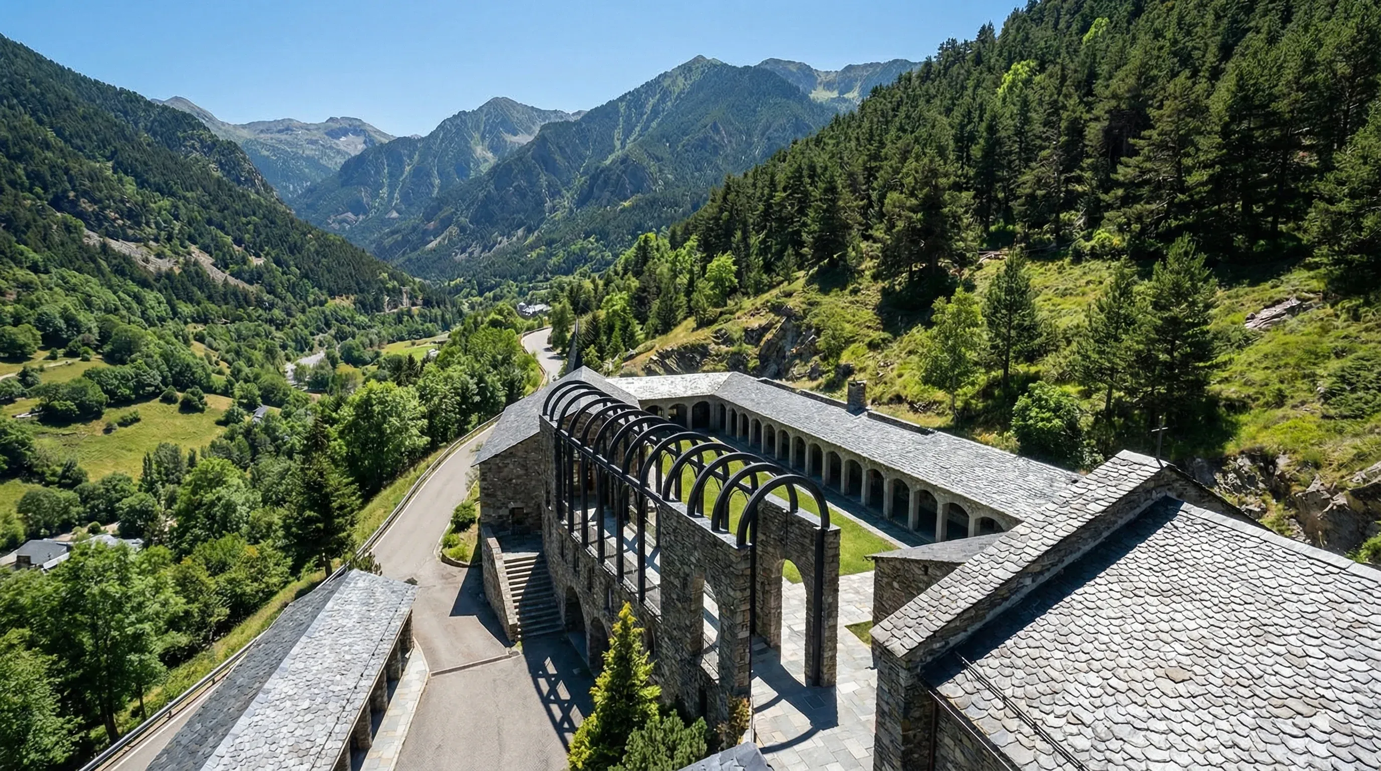 The stone and slate architecture of the Sanctuary of Meritxell is nestled in a green mountain valley under bright sunlight.