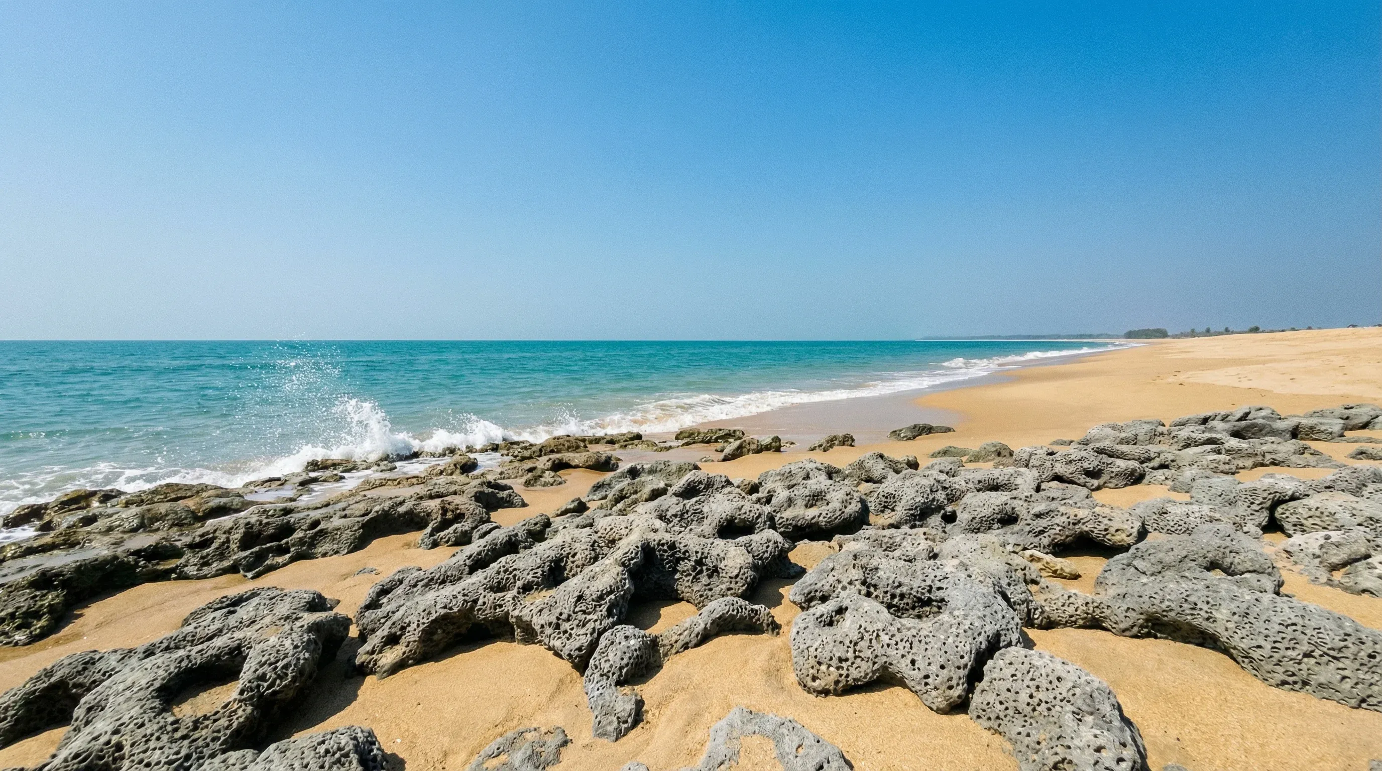 The sandy coastline of Inani Beach in Cox's Bazar, showing coral stone formations and the turquoise waters of the Bay of Bengal.