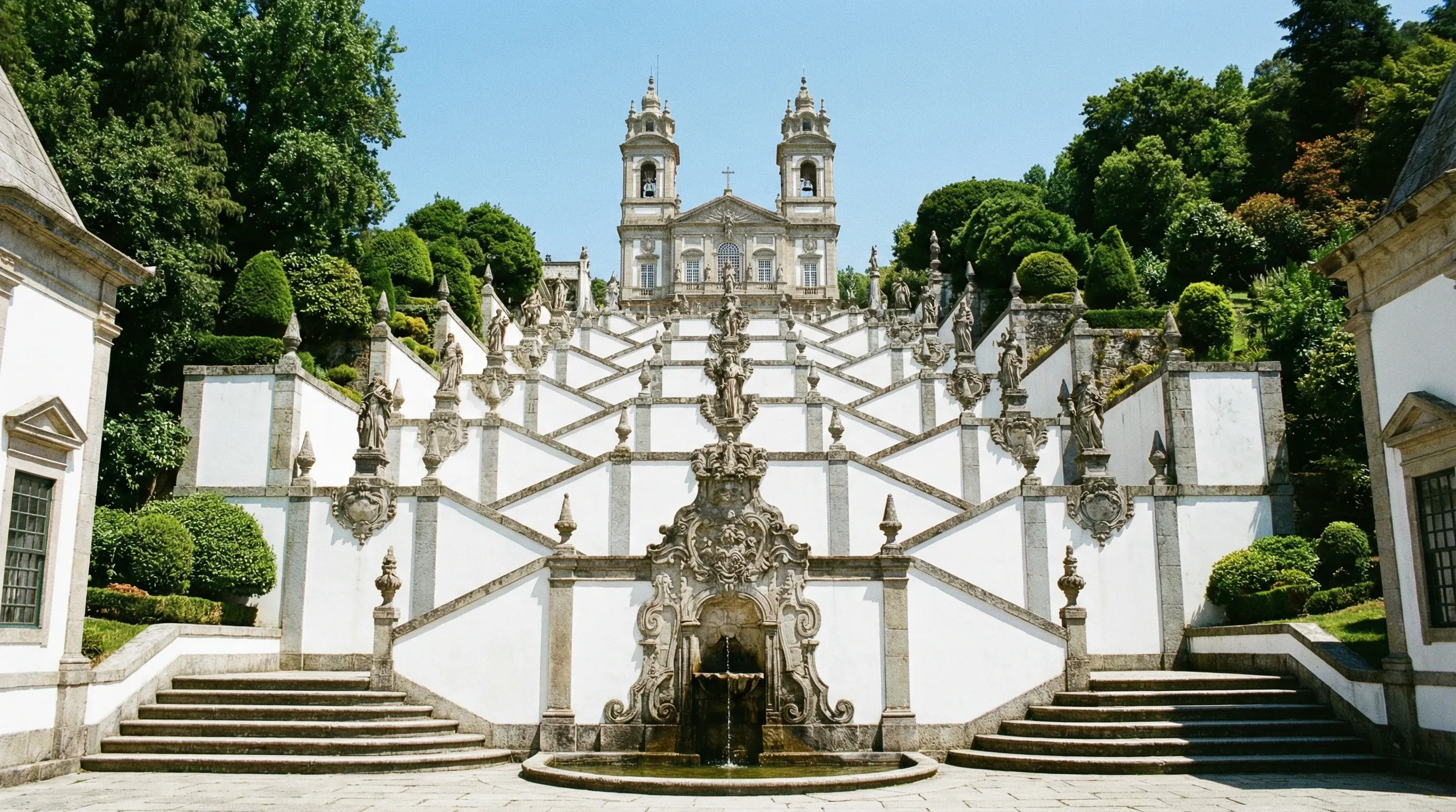 The Baroque zigzag stairway of the Sanctuary of Bom Jesus do Monte in Braga, surrounded by green trees.