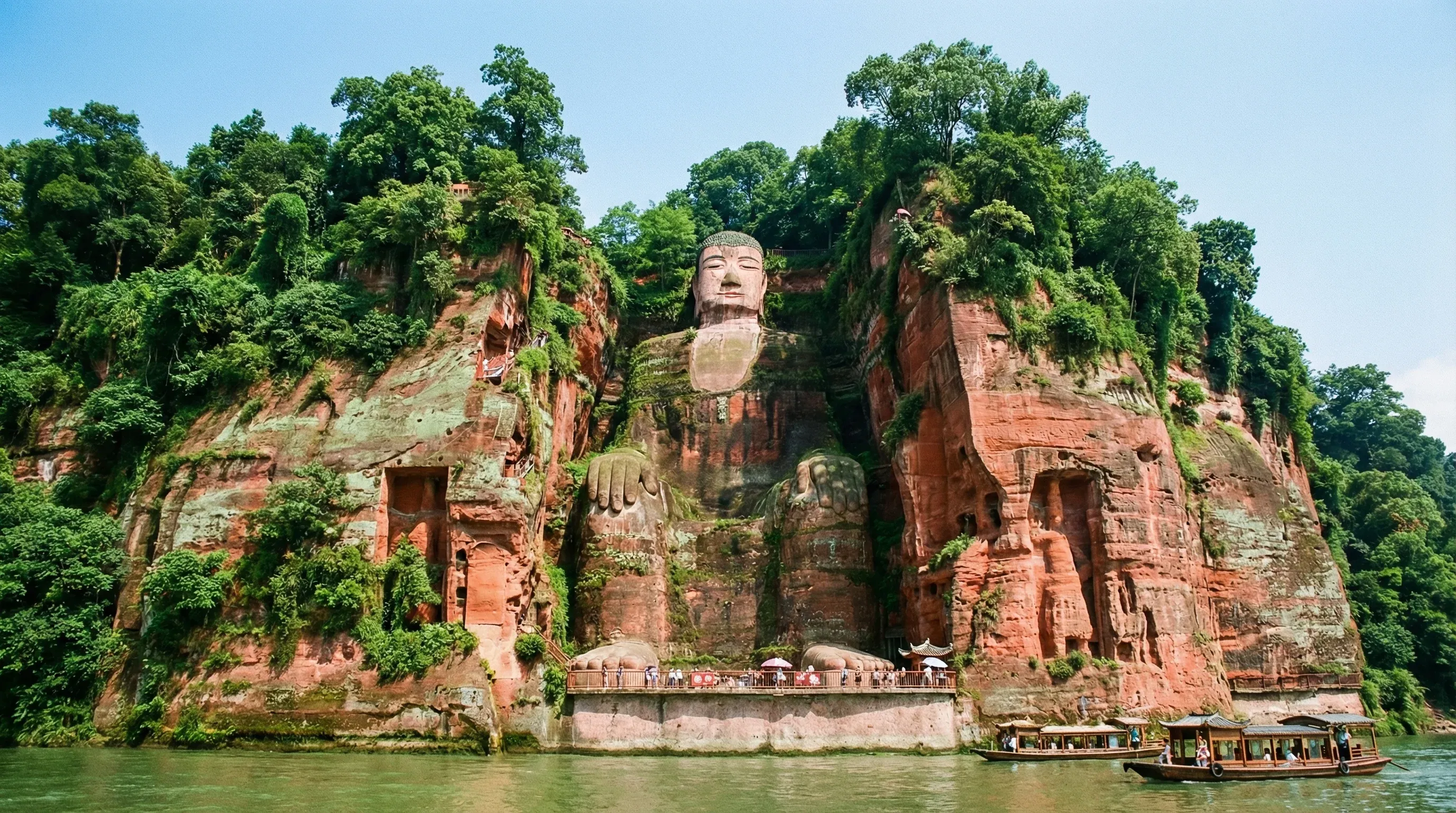 A massive stone Buddha statue carved into a red cliff face overlooking a river in Leshan.