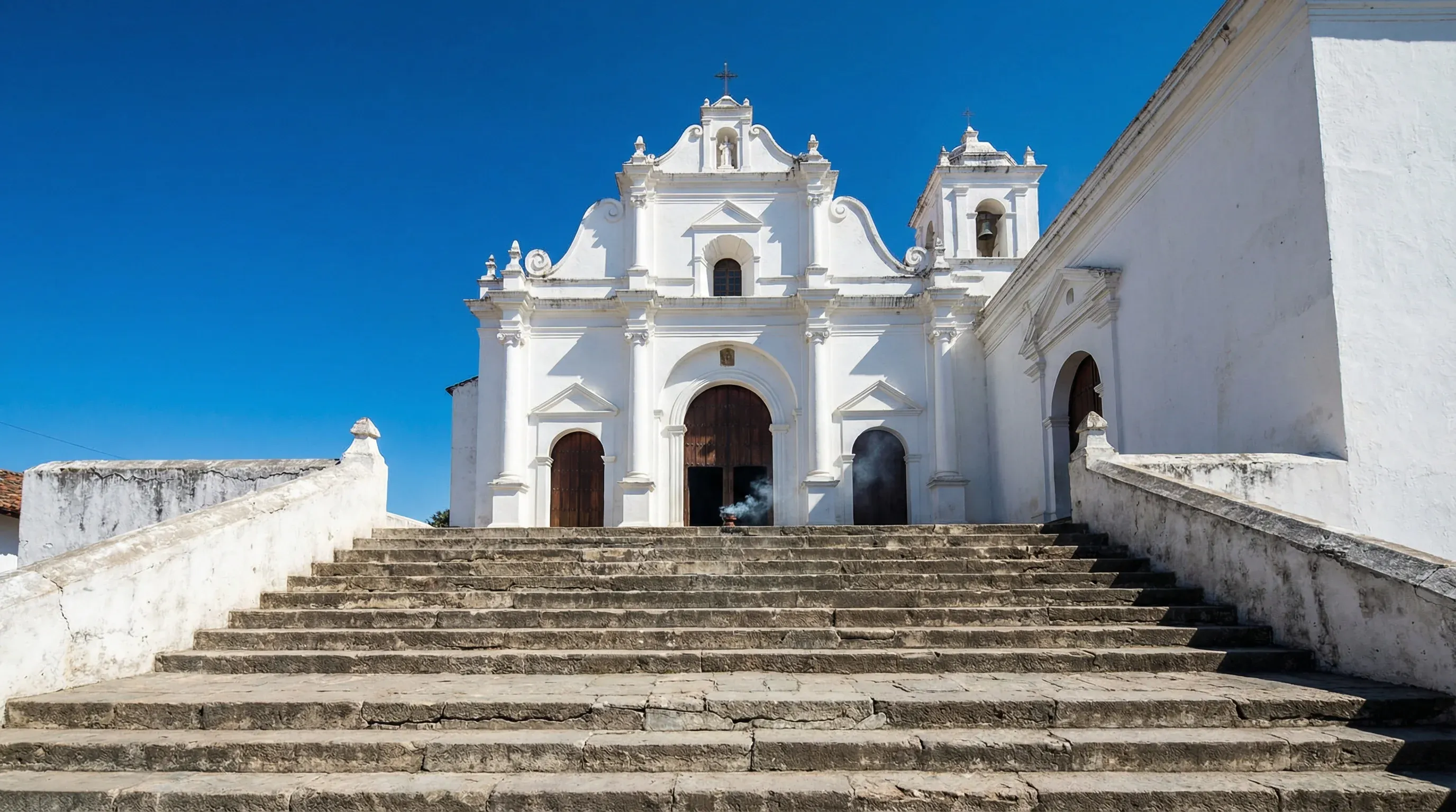The whitewashed facade and wide stone staircase of the colonial Iglesia de Santo Tomás in Chichicastenango.