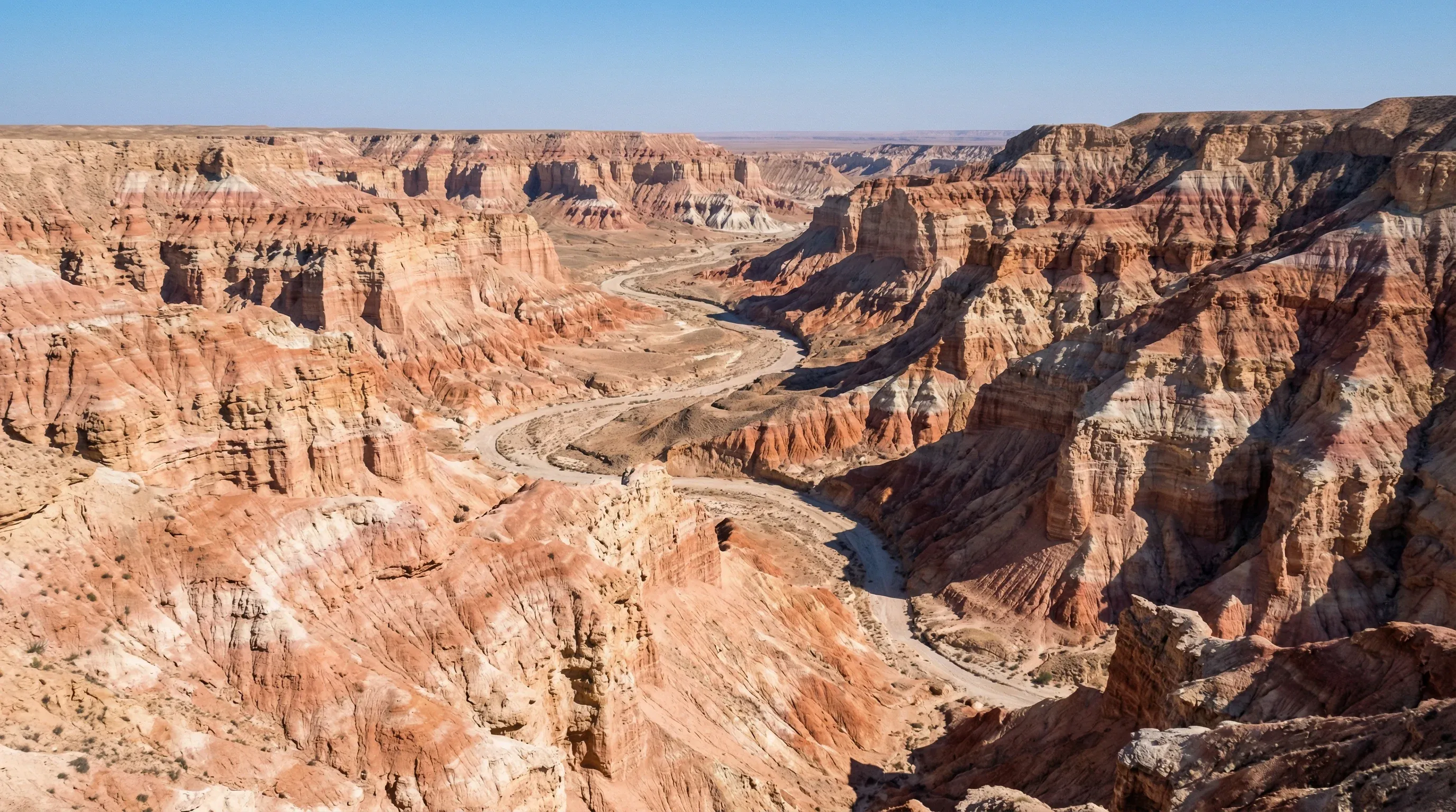 Multi-colored, layered rock formations and steep cliffs of Yangykala Canyon under a bright blue desert sky.