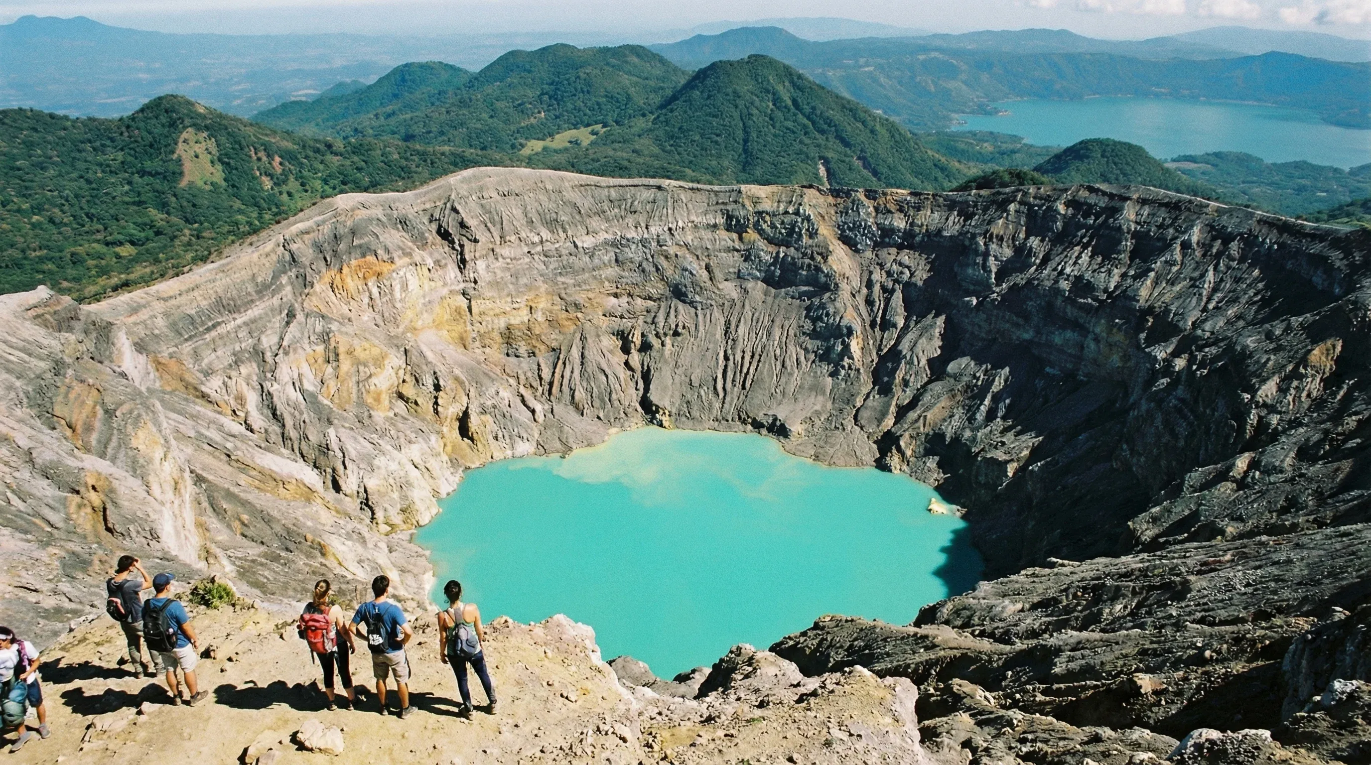 Aerial view into the crater of Santa Ana Volcano showing a bright turquoise sulfur lake and rocky walls.