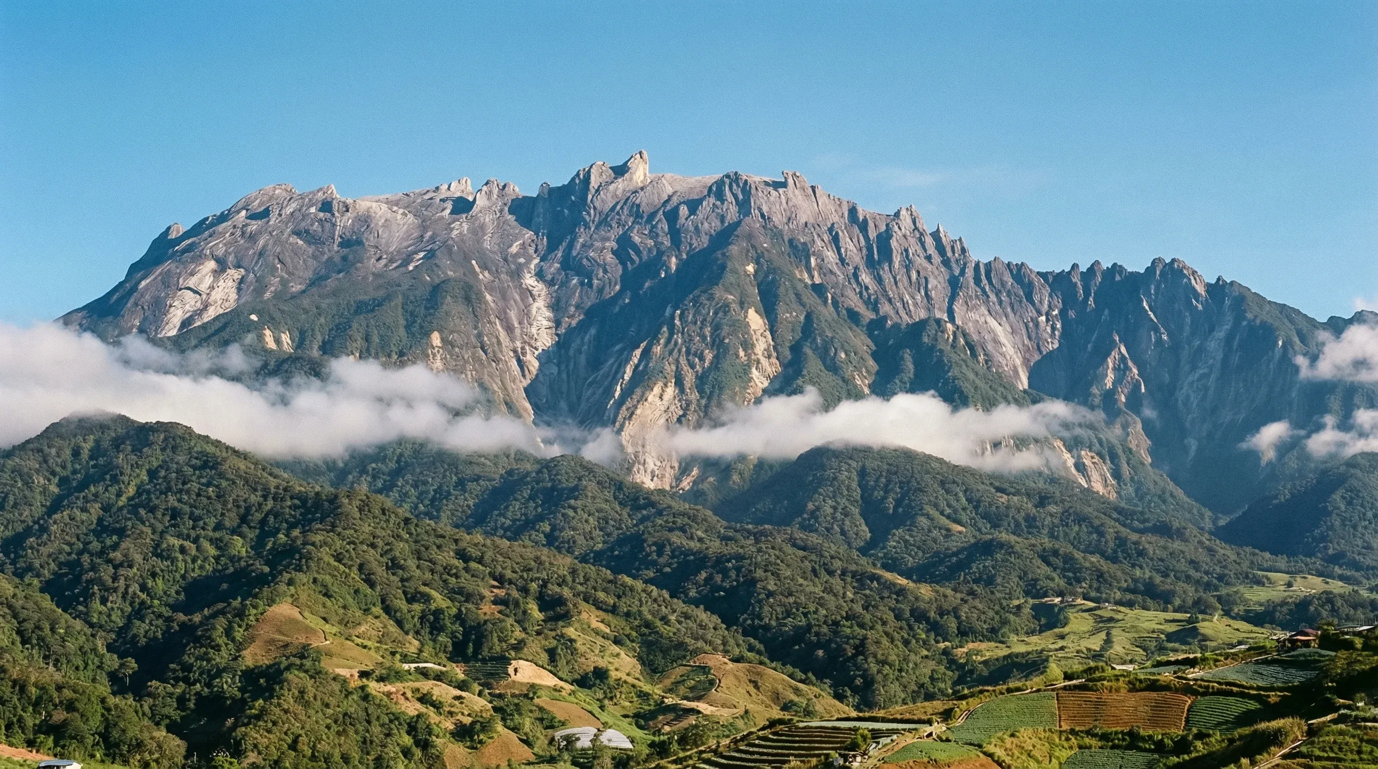 The jagged granite peaks of Mount Kinabalu rising above tropical forests and highland ridges in Sabah, Borneo.