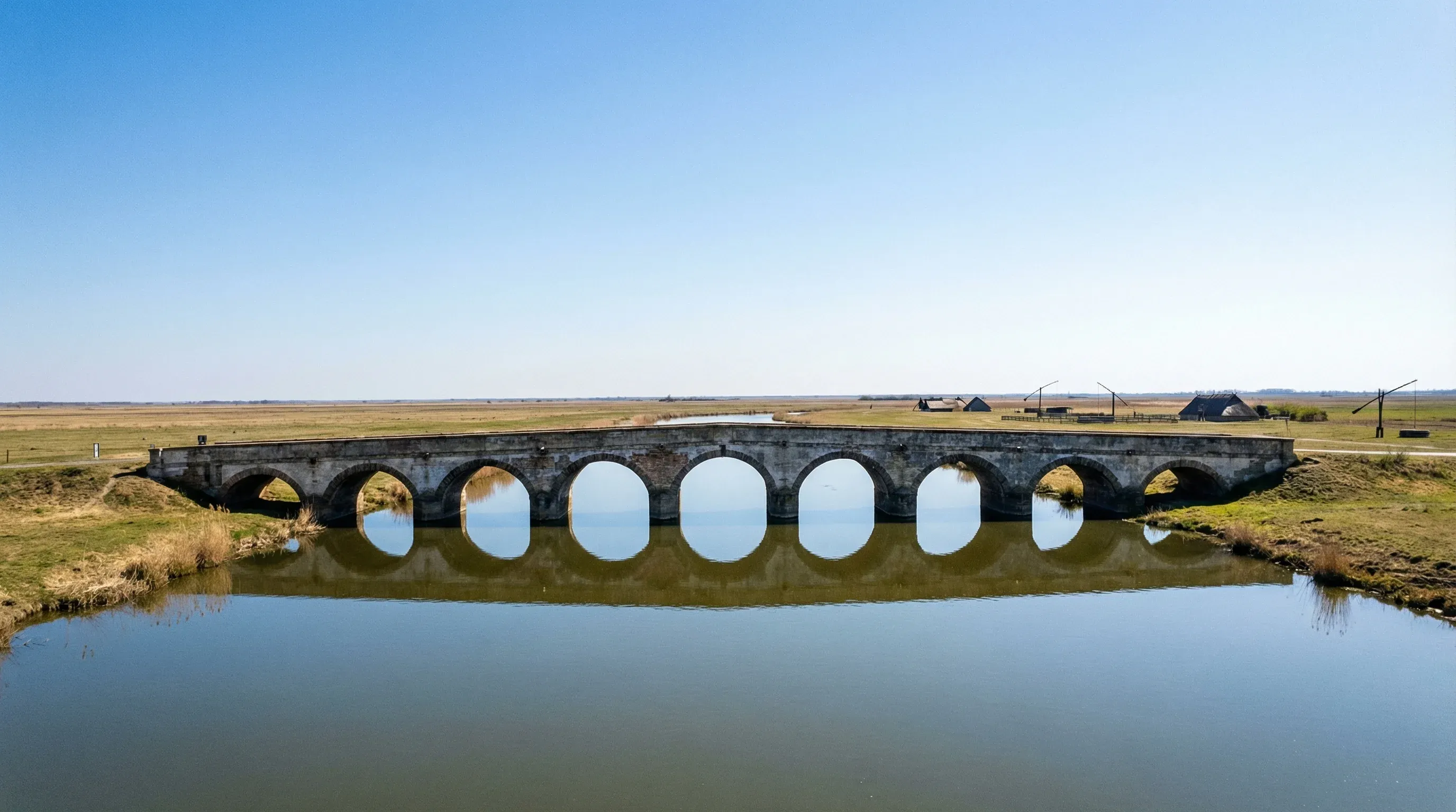 A long stone bridge with nine arches crossing a river in the flat grassland landscape of Hortobágy National Park.