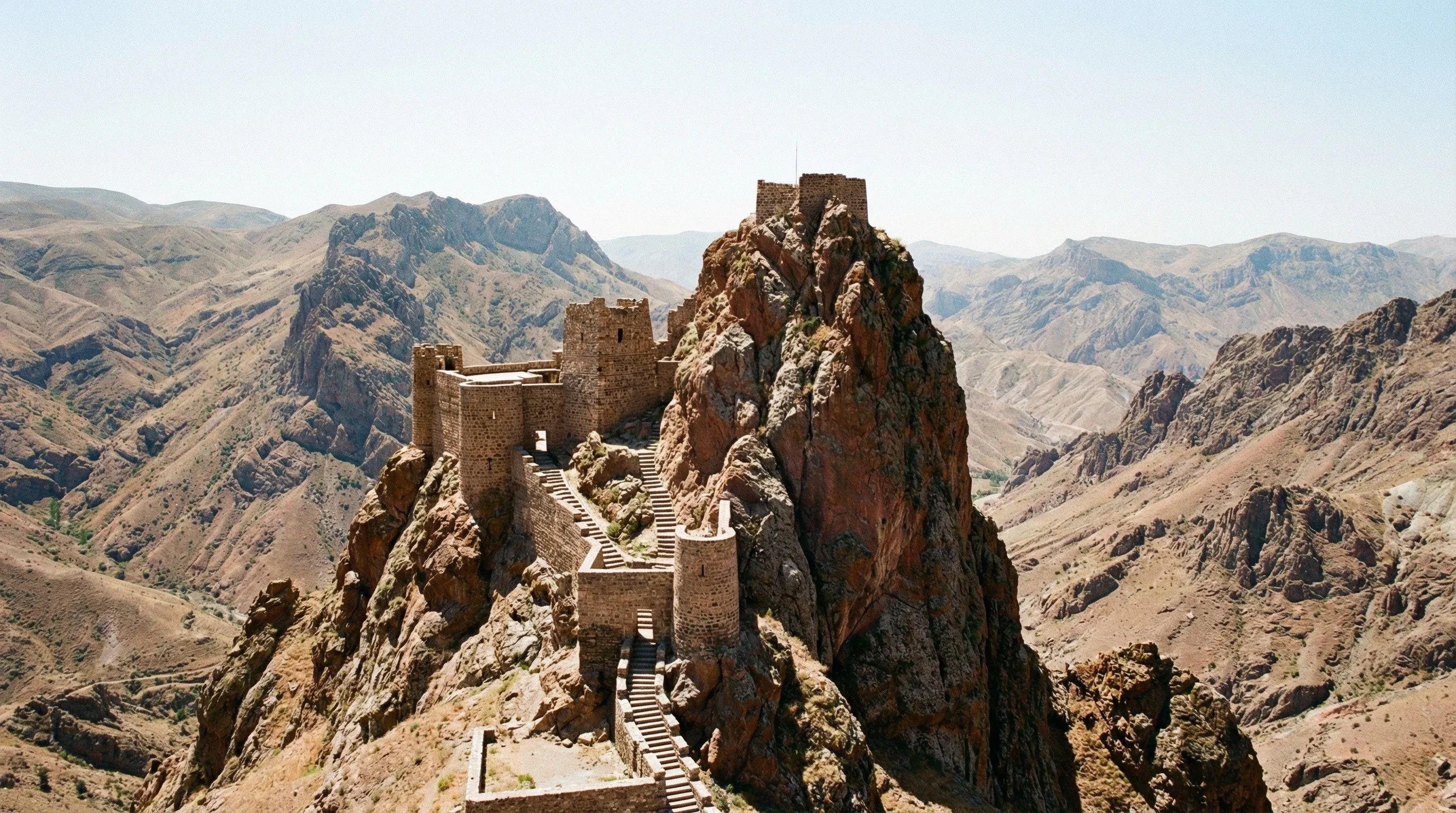 Stone walls and fortifications of Alinja Castle are built into the summit of a steep, rocky mountain peak in Nakhchivan.
