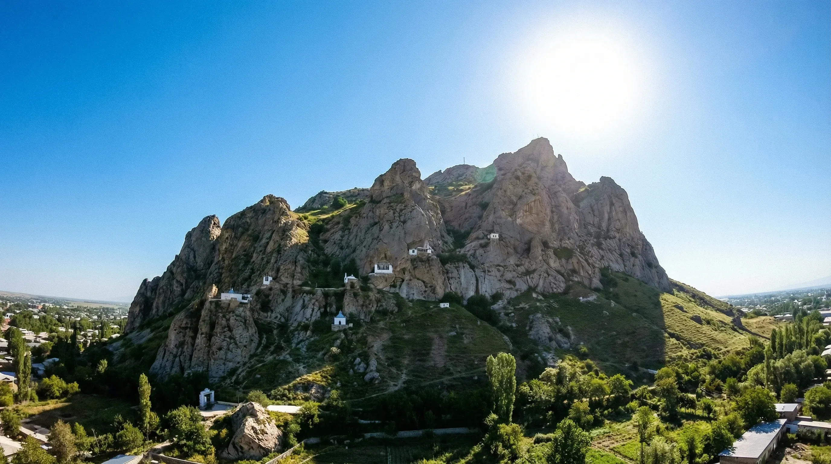 The craggy limestone peaks of Sulaiman-Too Mountain rising above the city of Osh under a bright sun.