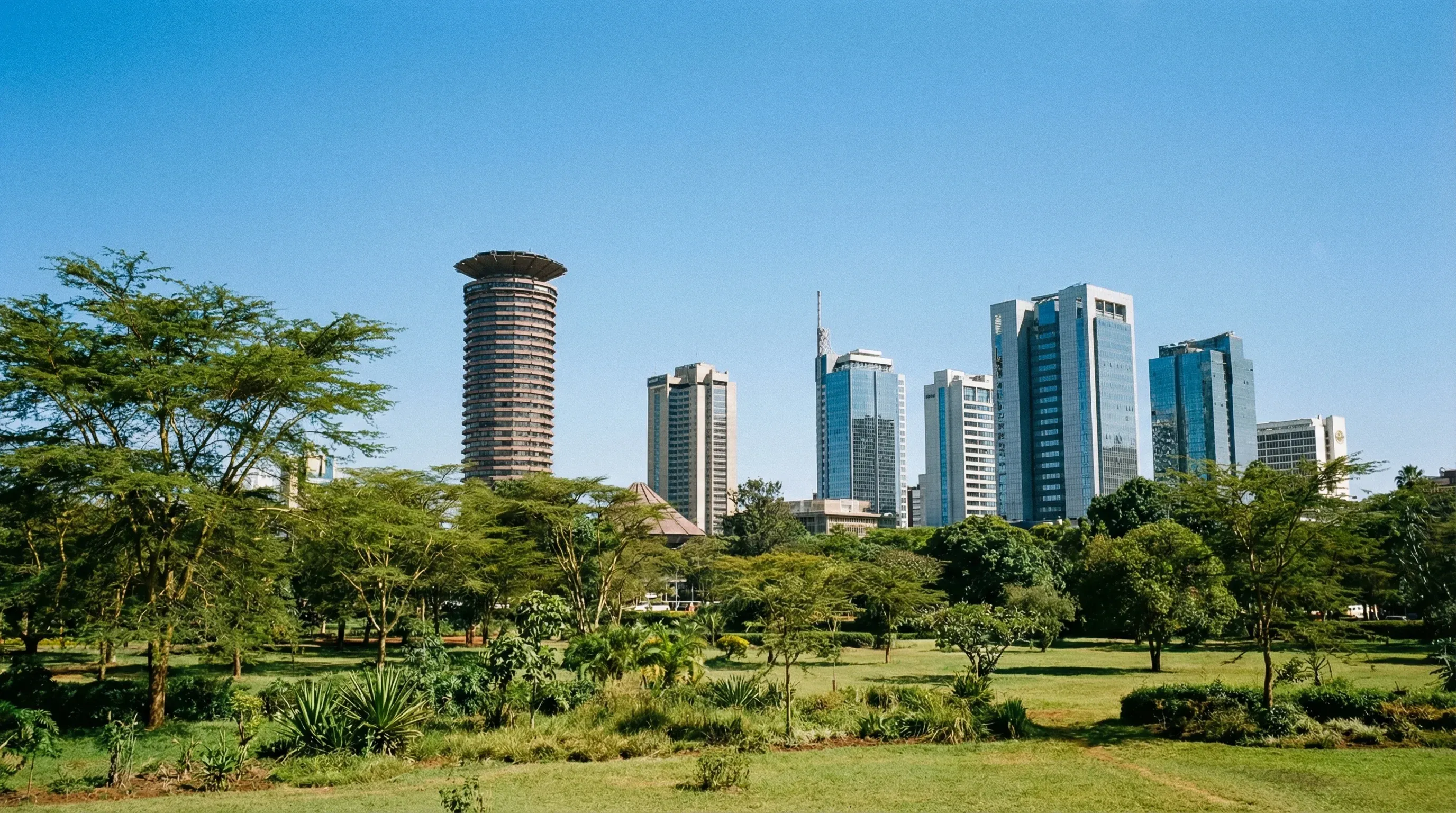 The modern skyscrapers of Nairobi's central business district seen behind the green trees and lawns of Uhuru Park.