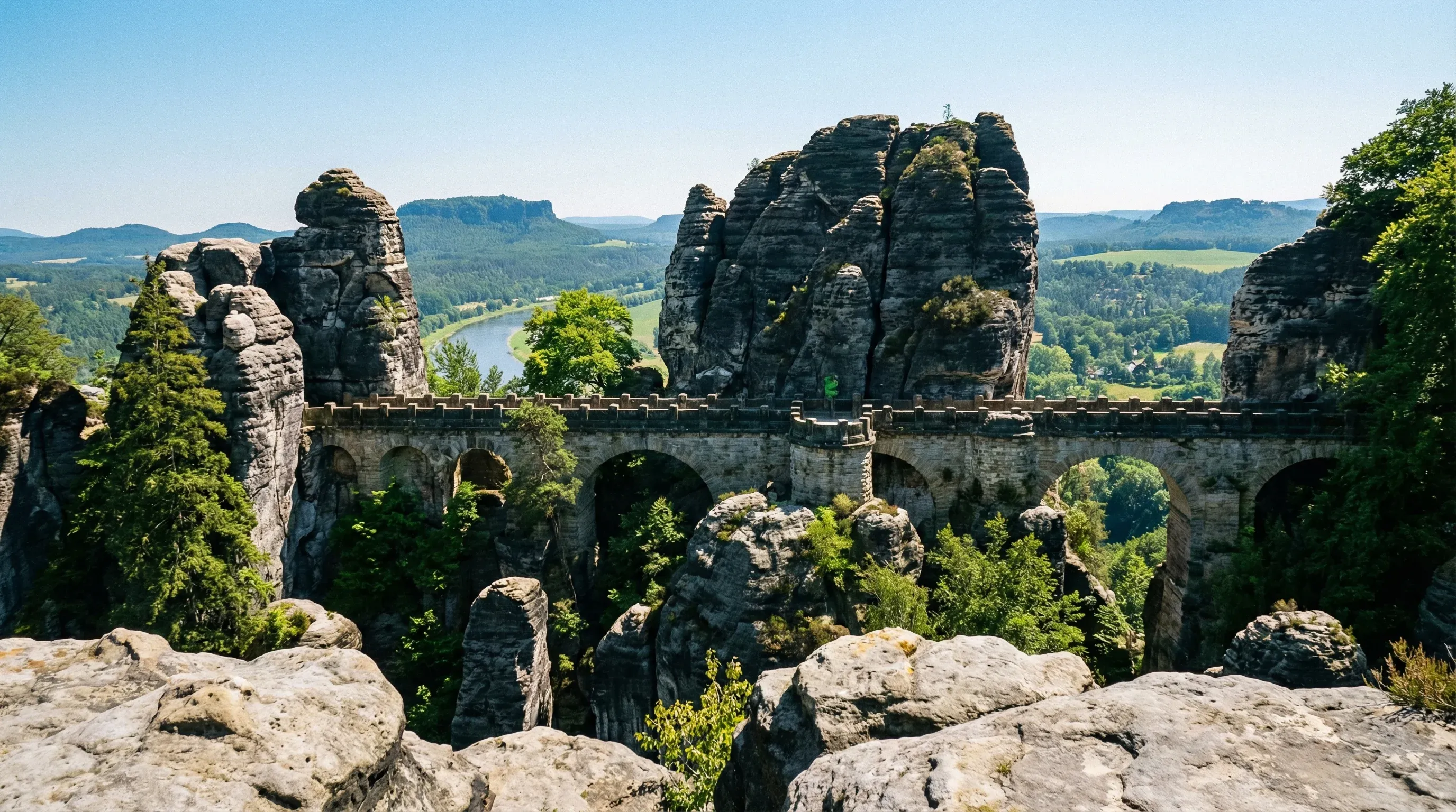 A stone bridge connects jagged sandstone rock formations in the Saxon Switzerland mountains.