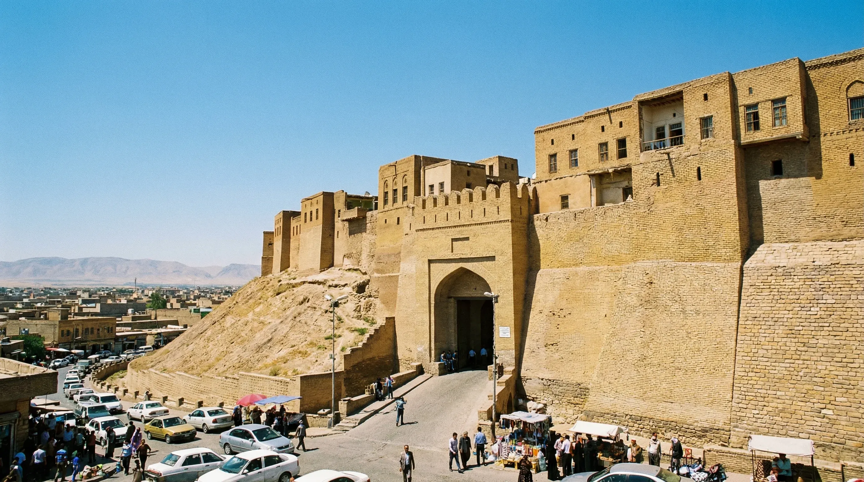 An ancient fortified city with high brick walls on a large hill under a bright blue sky.