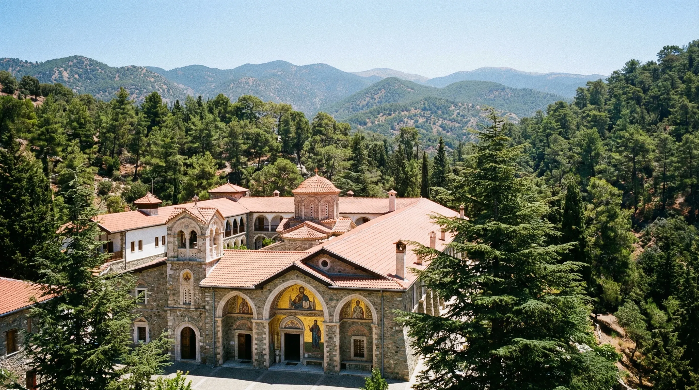 The stone exterior and arched walkways of Kykkos Monastery surrounded by the green pine forests of the Troodos Mountains.
