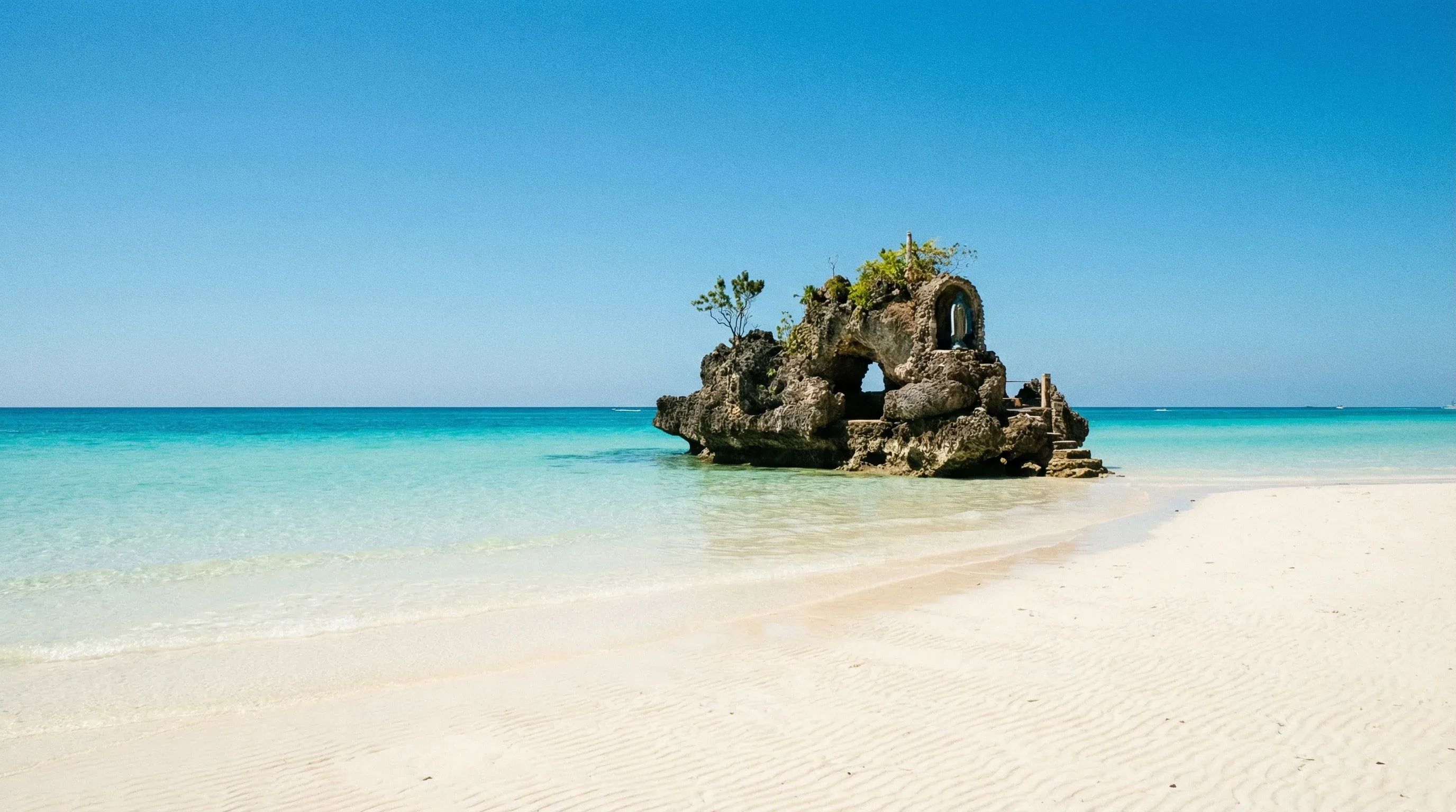 A clear white sand beach with turquoise water and a volcanic rock formation offshore in Boracay.