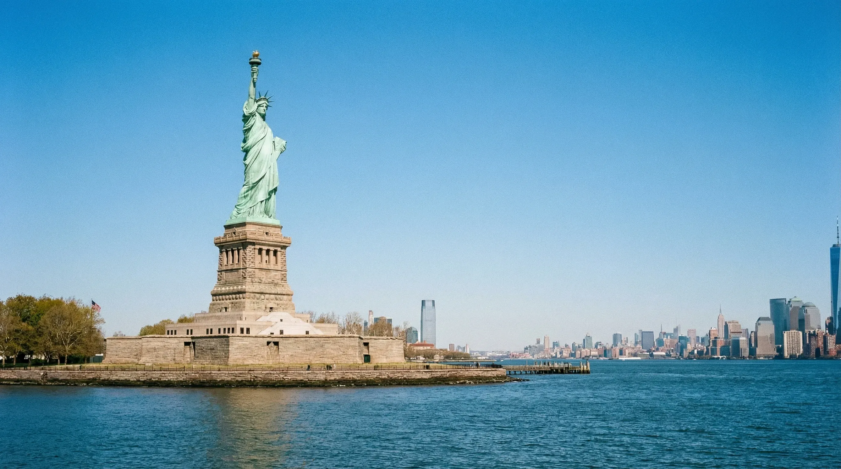 The Statue of Liberty standing on its pedestal in New York Harbor under a clear blue sky.