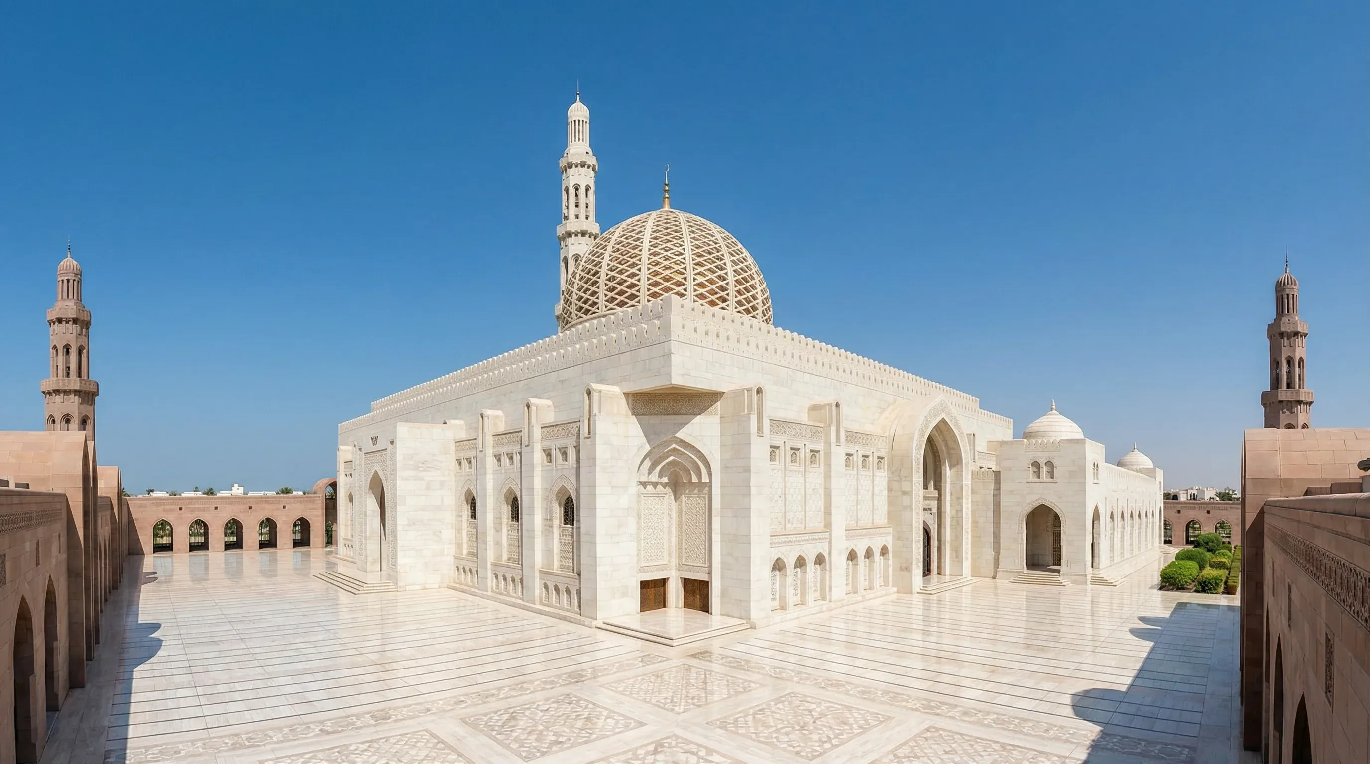 The white marble facade, central dome, and minaret of the Sultan Qaboos Grand Mosque in Muscat under a clear sky.