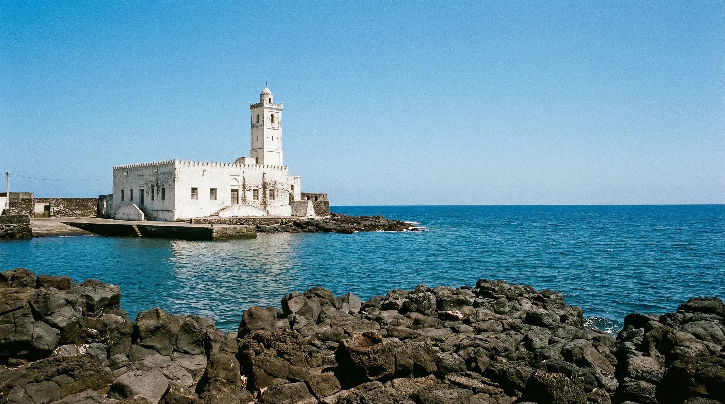 The iconic white Friday Mosque standing on a rocky volcanic shoreline next to the turquoise sea in Moroni, Grande Comore.