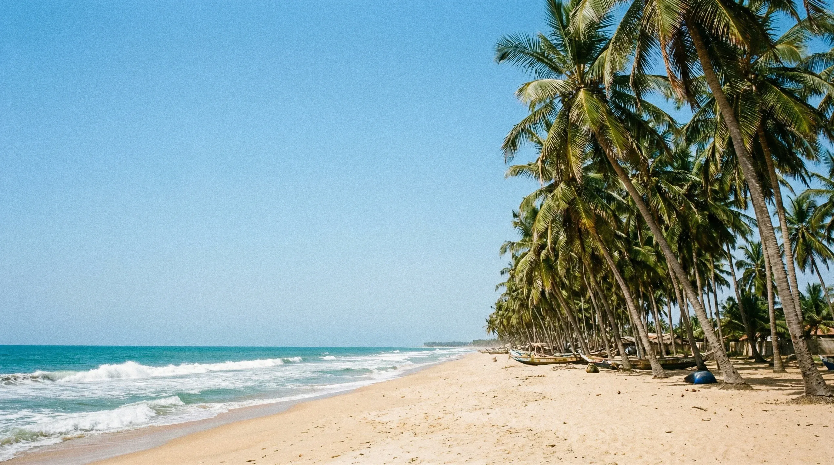 A palm-fringed sandy beach along the Gulf of Guinea in Lomé, featuring clear blue water and bright sunlight.