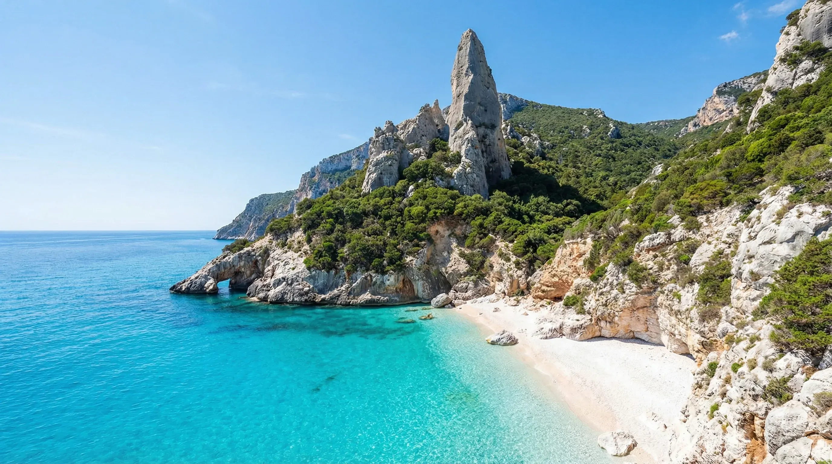 A towering limestone rock spire next to a white pebble beach and turquoise water at Cala Goloritzé.