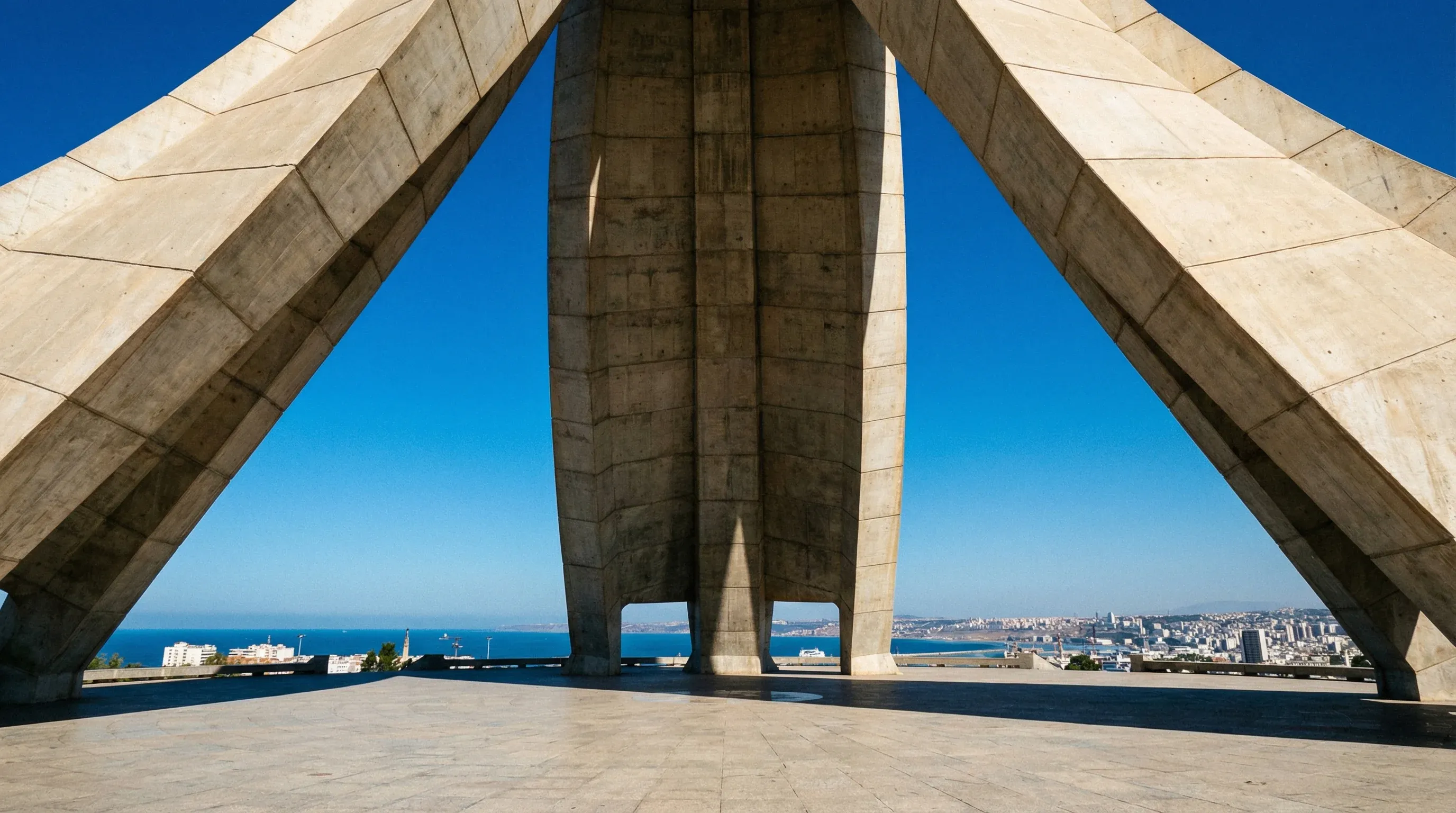The Maqam Echahid monument in Algiers, featuring three massive concrete palm leaves reaching toward a clear blue sky.