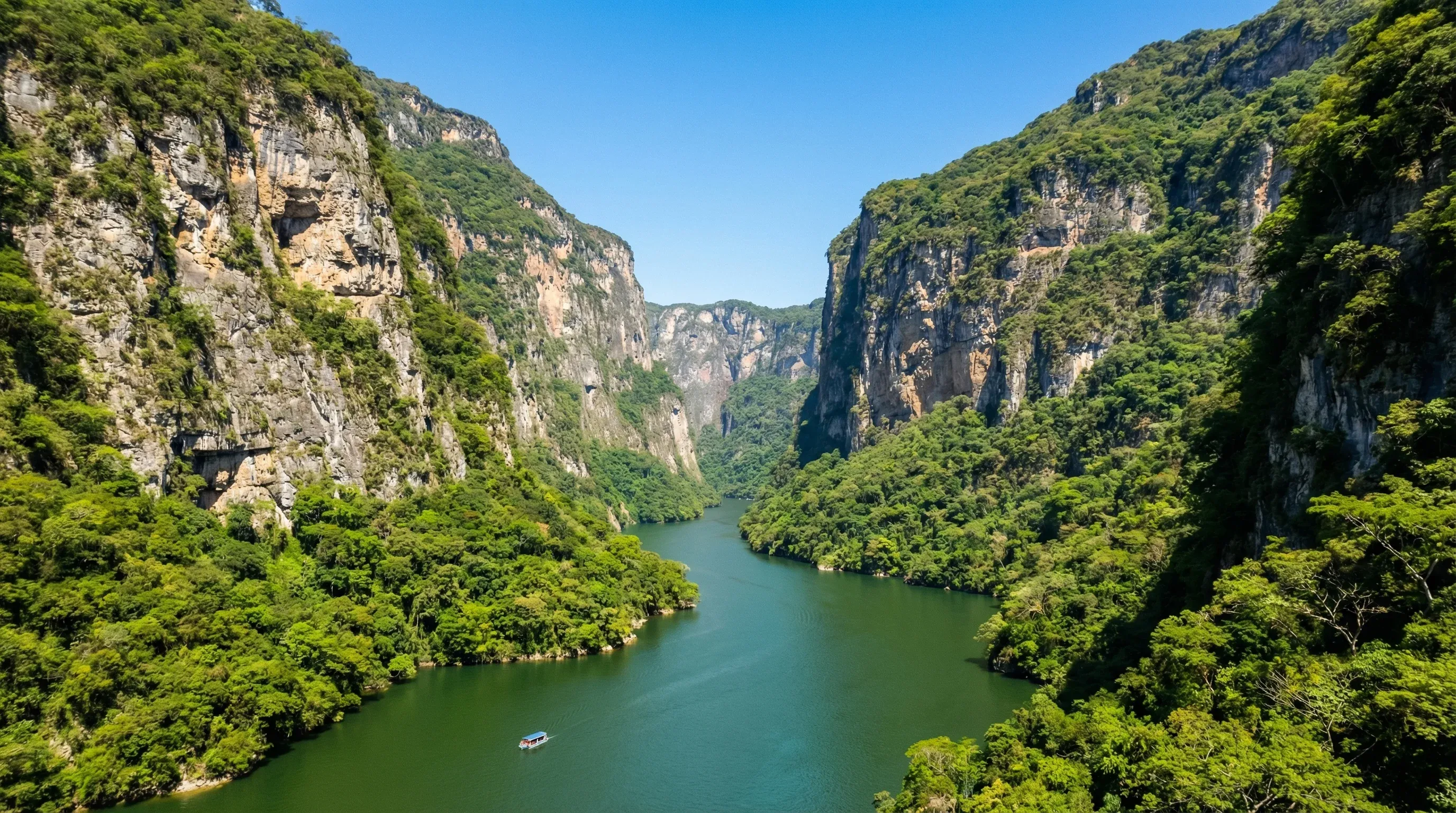 High vertical limestone cliffs covered in green foliage line the Grijalva River in the Sumidero Canyon.