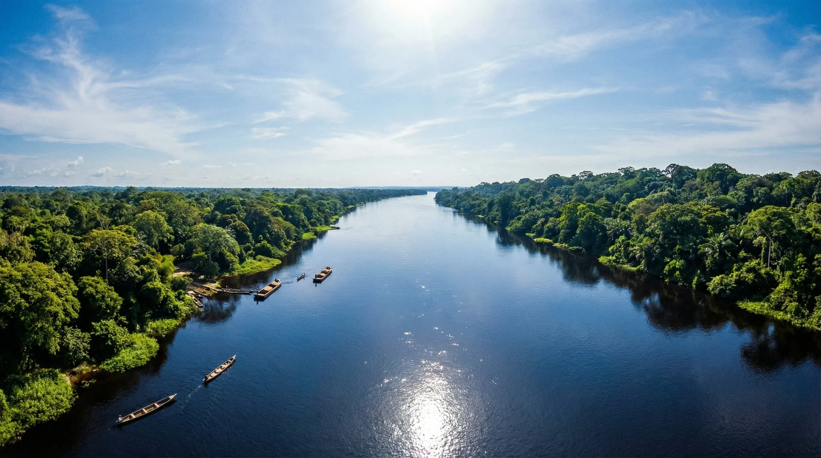 A wide view of the expansive Congo River lined with dense green rainforest under a clear blue sky.