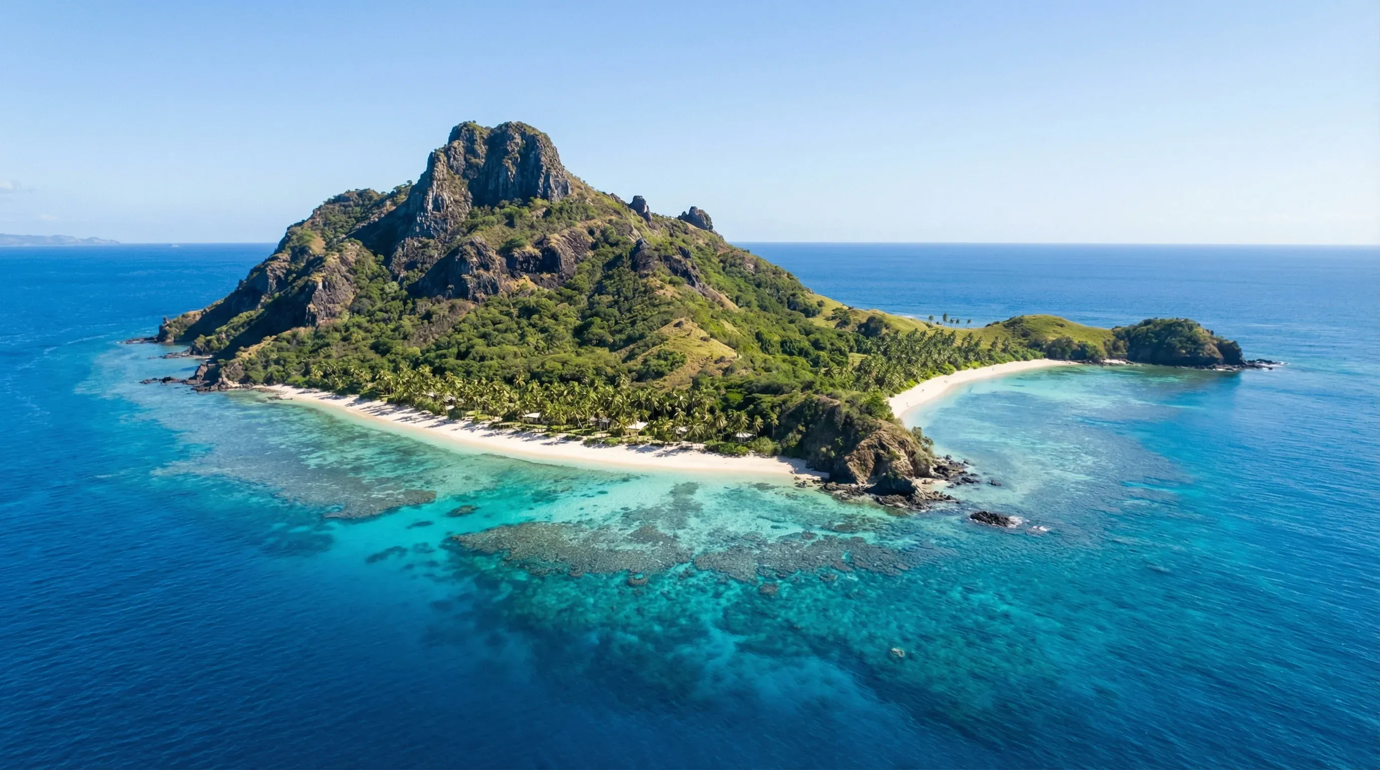 Aerial view of Monuriki Island in the Mamanuca Islands, showing white sand beaches, volcanic cliffs, and surrounding coral reefs in turquoise water.