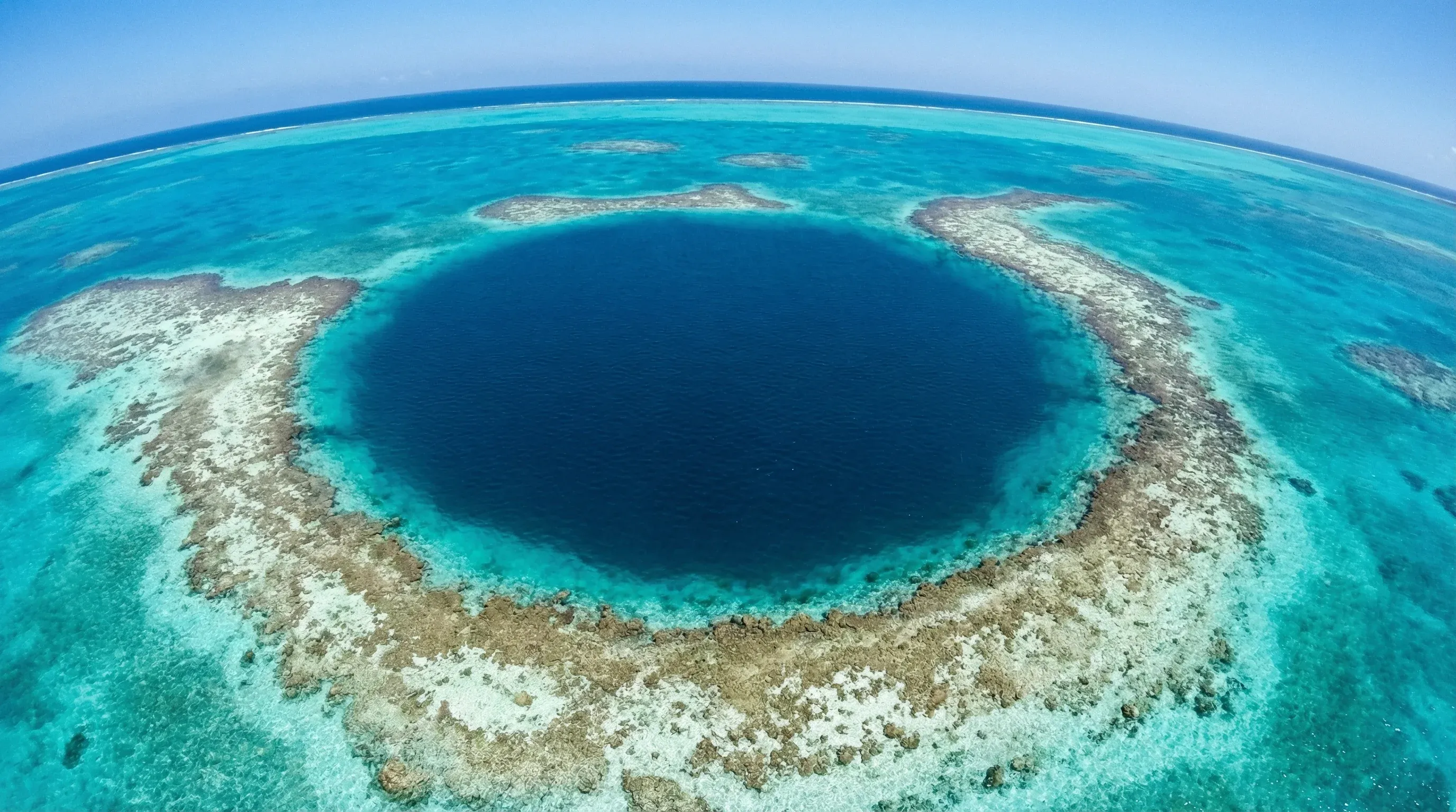 Aerial view of the Great Blue Hole, a large circular marine sinkhole surrounded by turquoise coral reefs in the Belize Barrier Reef.
