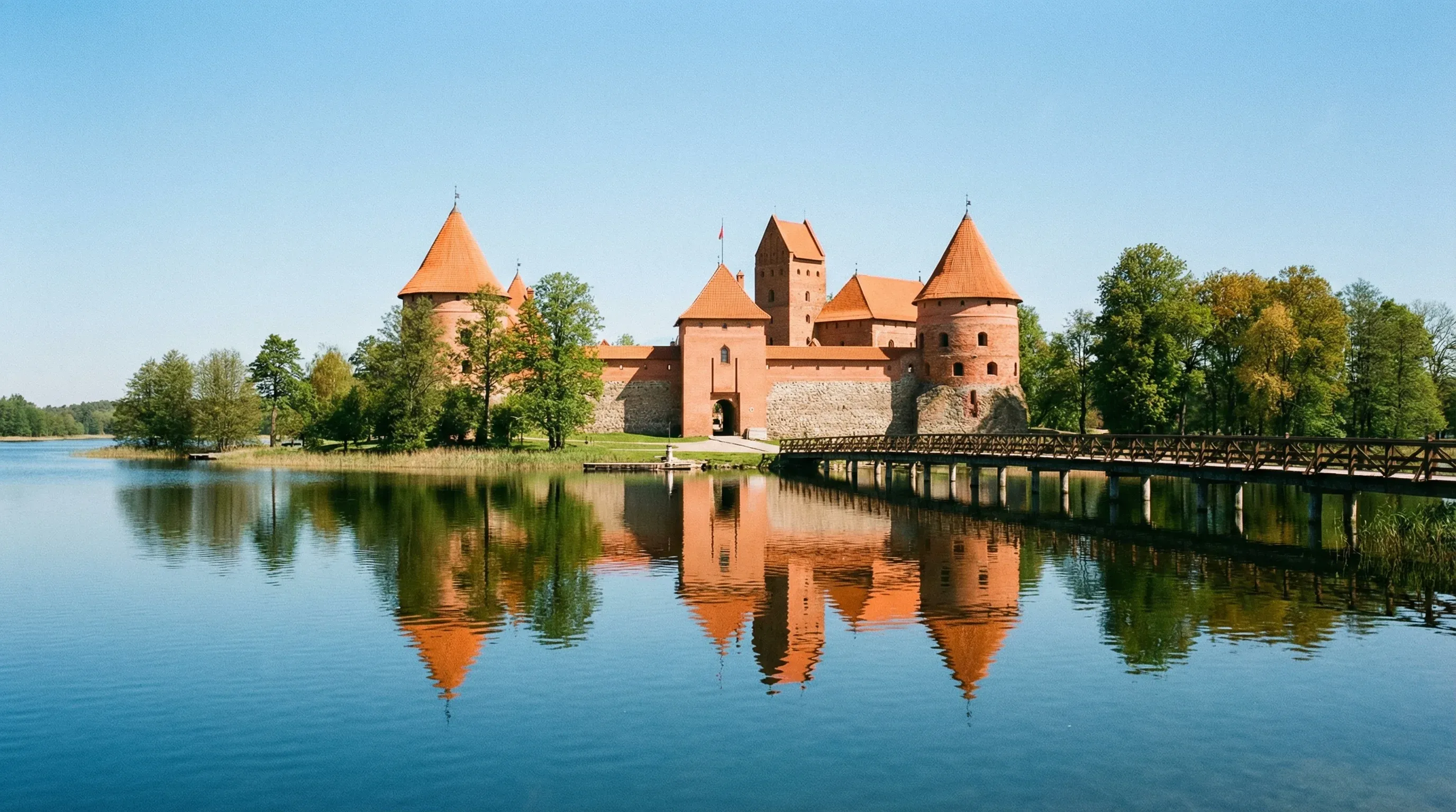 The red-brick Trakai Island Castle situated on Lake Galvė, connected by a wooden bridge under a clear sky.
