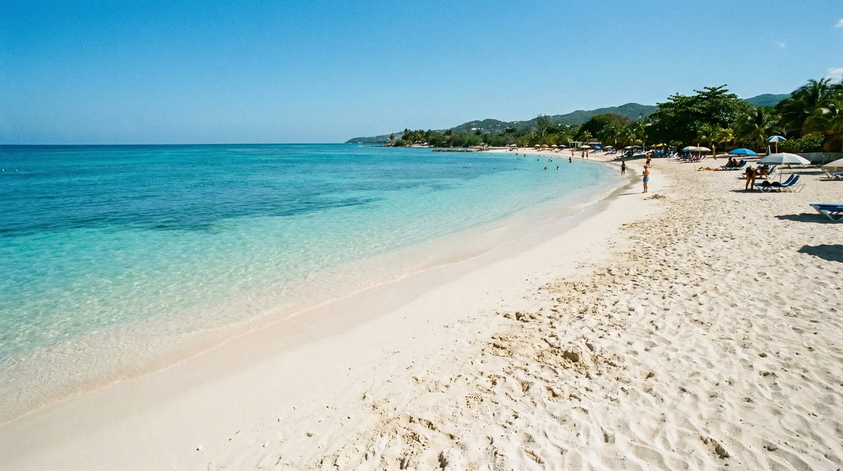 A photograph of the white sand beach and clear turquoise Caribbean Sea at Doctor's Cave Beach in Montego Bay.
