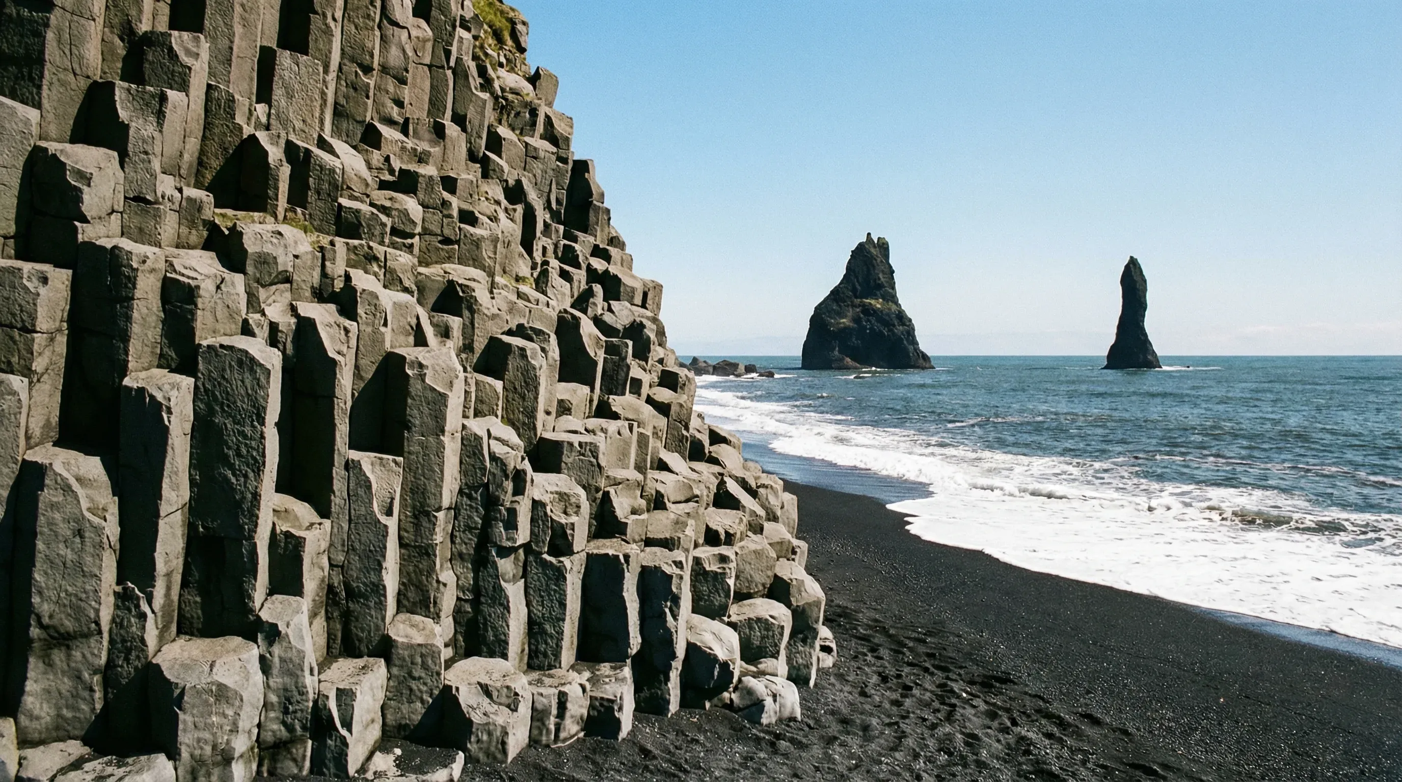 The black sand beach of Reynisfjara in South Iceland, featuring hexagonal basalt columns and sea stacks in the ocean.