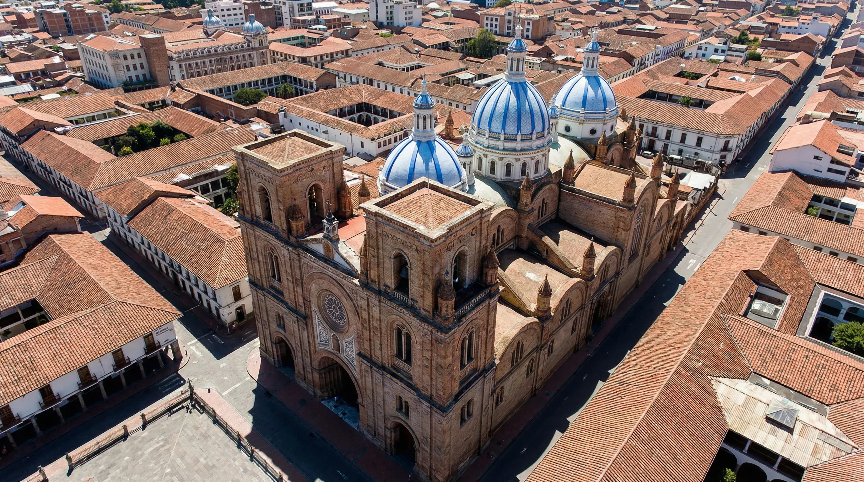 The blue-and-white tiled domes of a large brick cathedral rise above the red-tiled rooftops of a colonial city.
