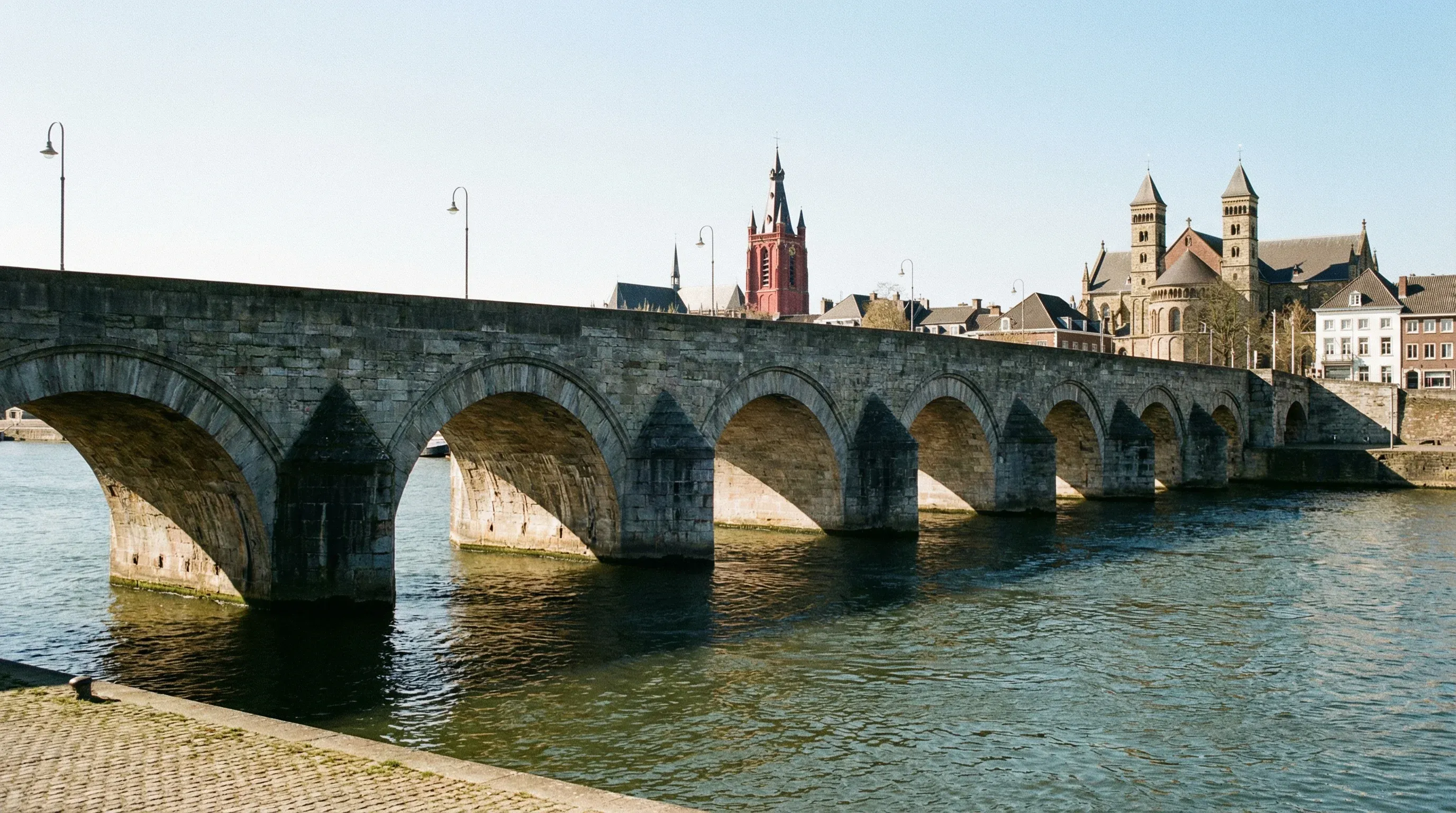 The historic stone arches of the Sint Servaasbrug bridge over the Maas River in Maastricht, Netherlands.
