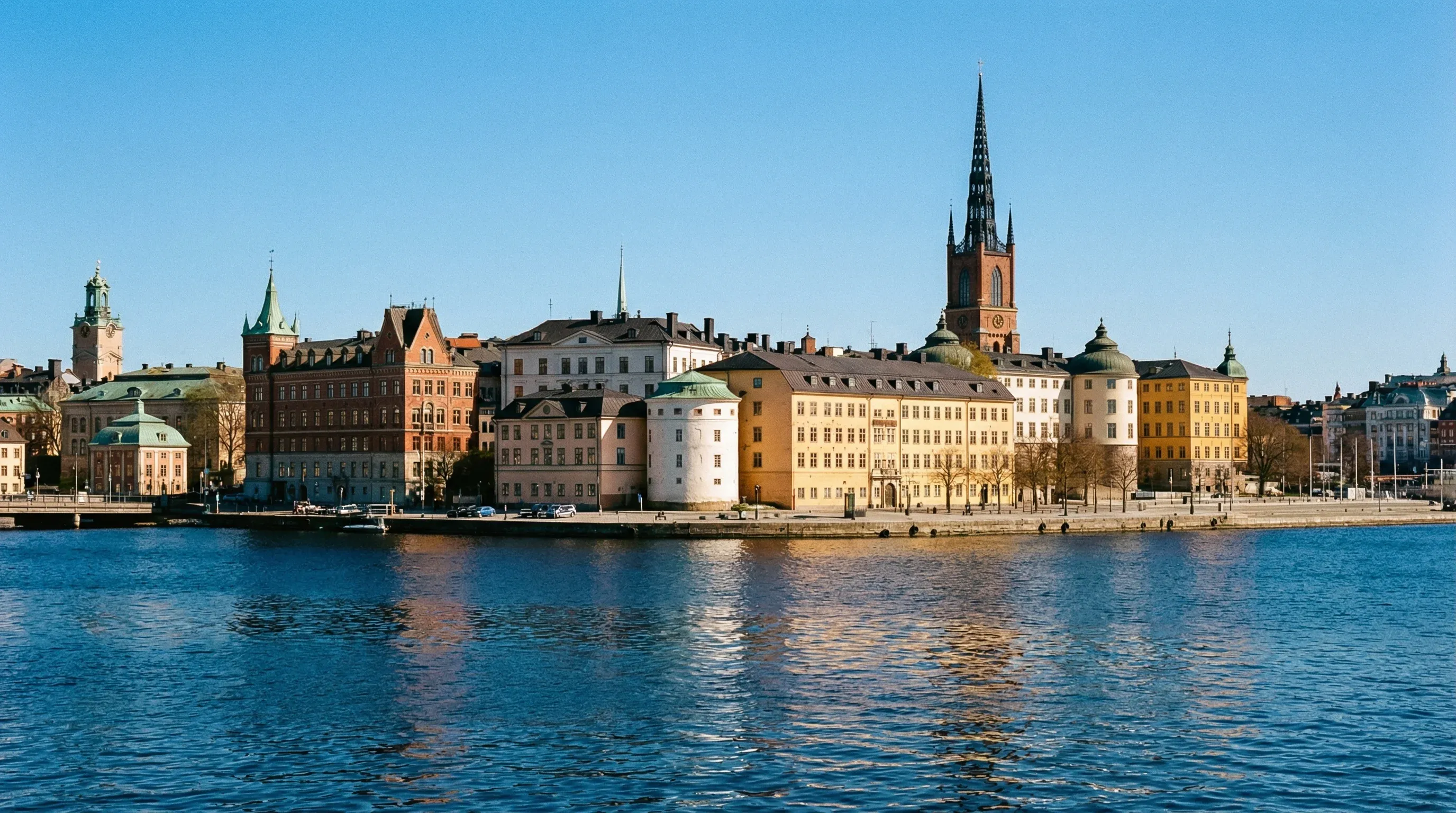 Historic colorful buildings and a cathedral spire along the waterfront of Stockholm's Old Town.