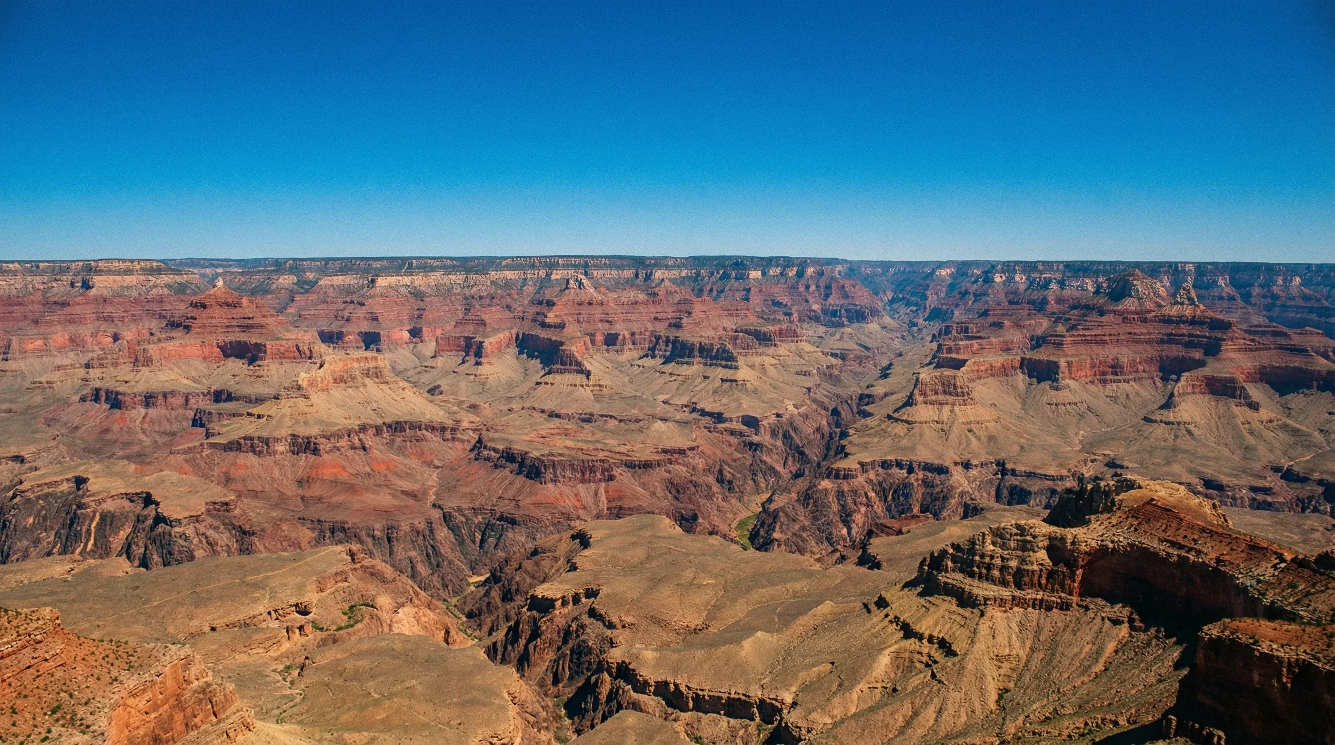 A vast view of the layered red rock formations of the Grand Canyon under a clear blue sky.