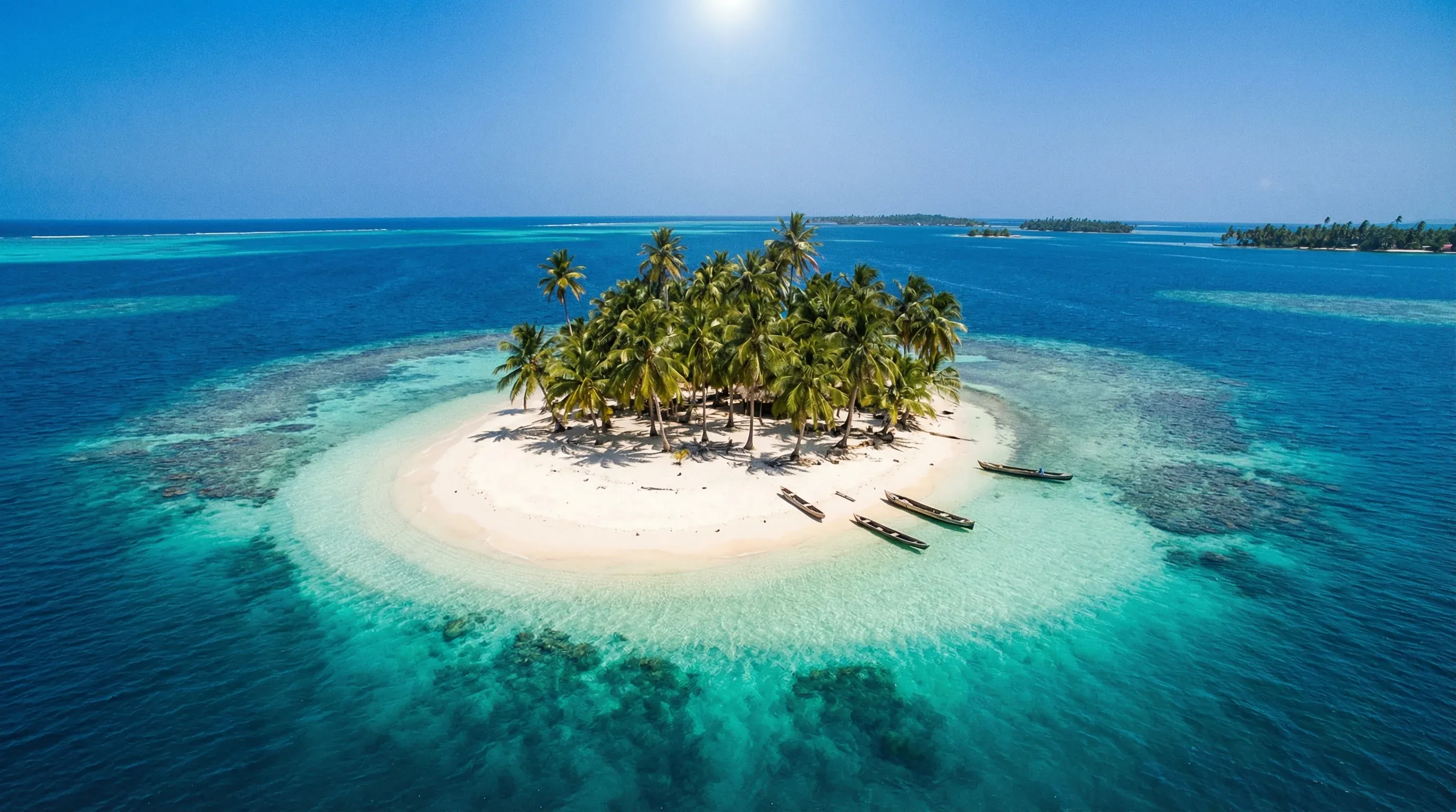 A small island with white sand and palm trees surrounded by clear, multi-toned blue water.