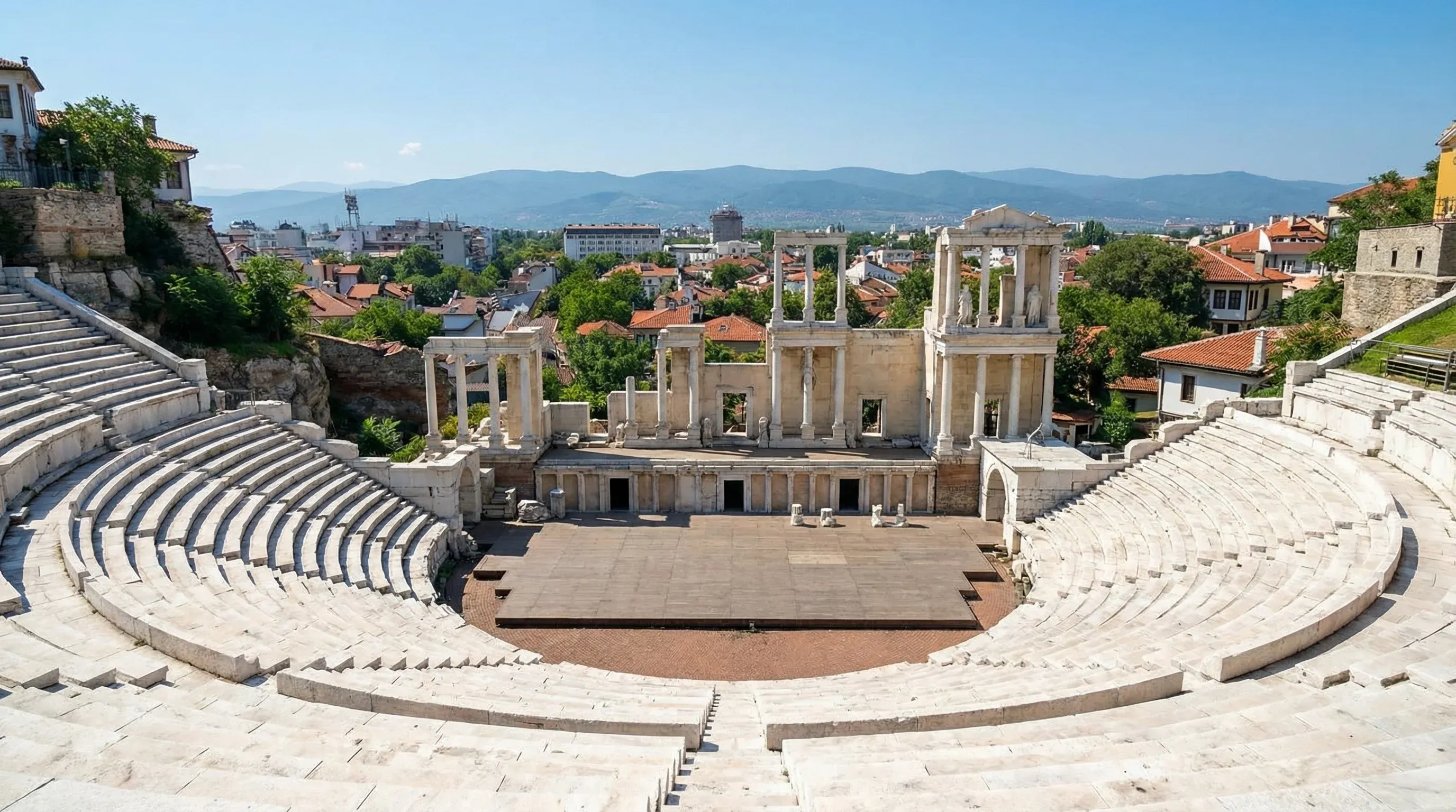 A view of the ancient Roman theatre in Plovdiv, Bulgaria, showing the marble seating and the stage columns under a blue sky.