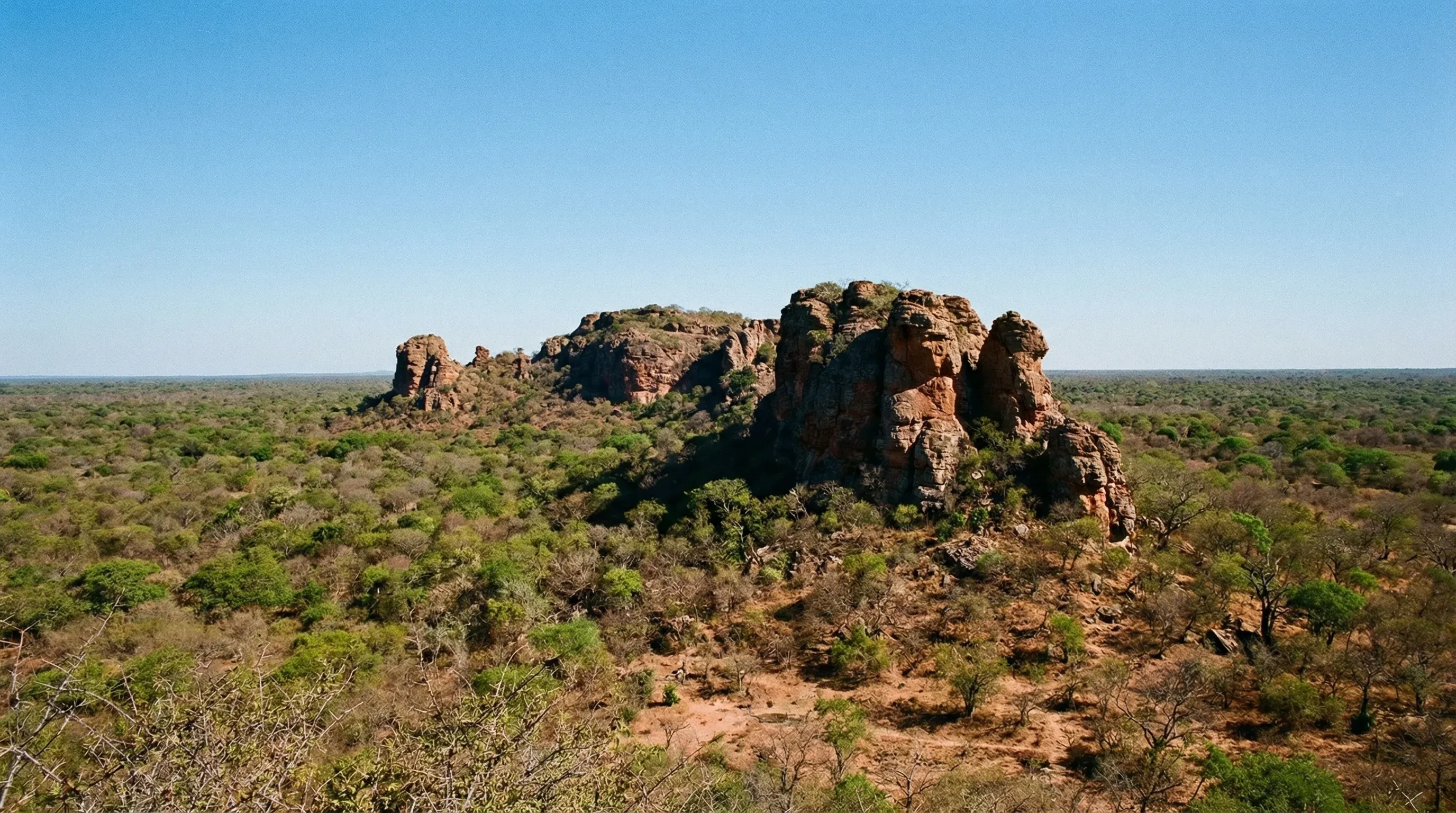 Rugged rock hills rising from a vast, dry green forest under a bright clear sky in the Gran Chaco.