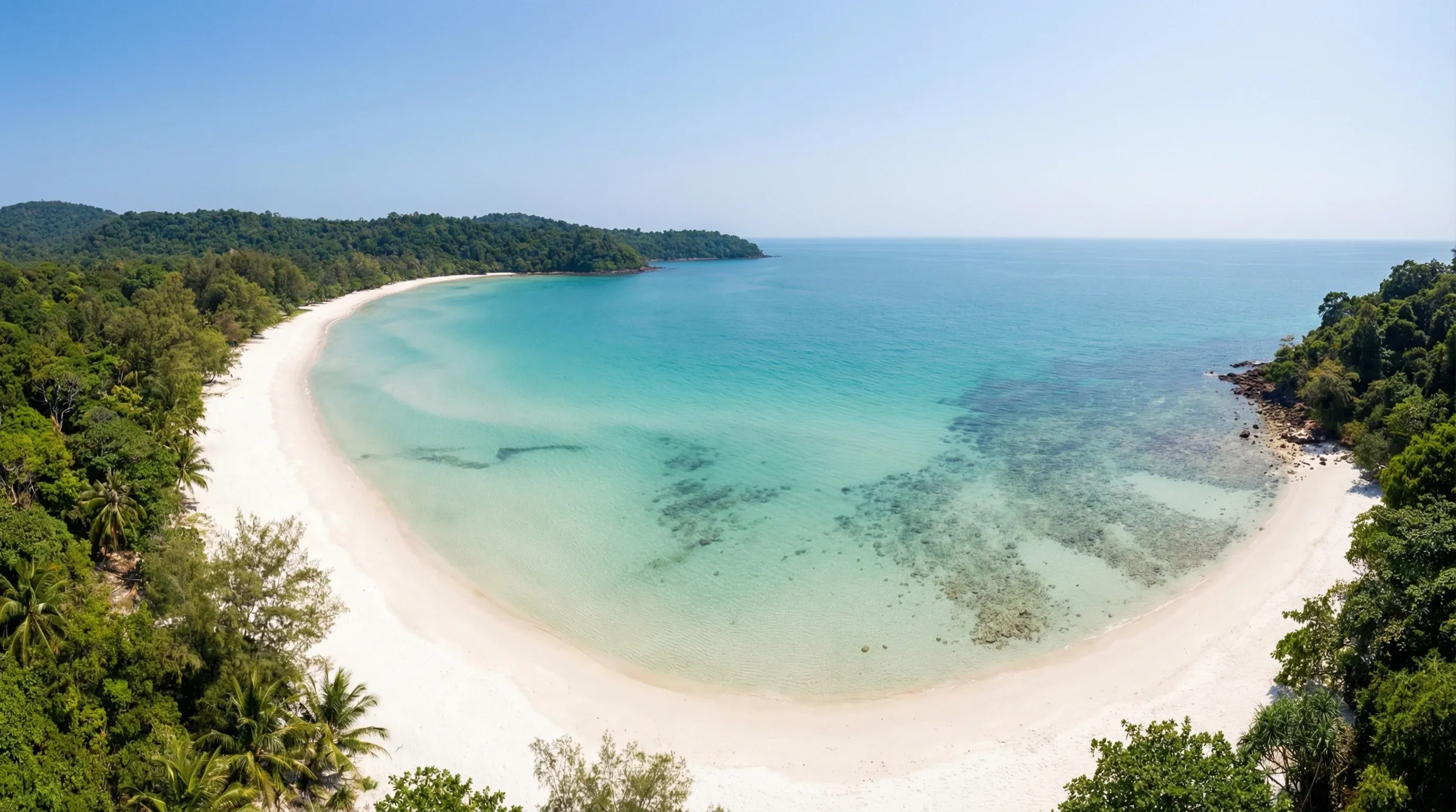 A wide white sand beach and turquoise ocean bay surrounded by tropical jungle on Koh Rong Sanloem.