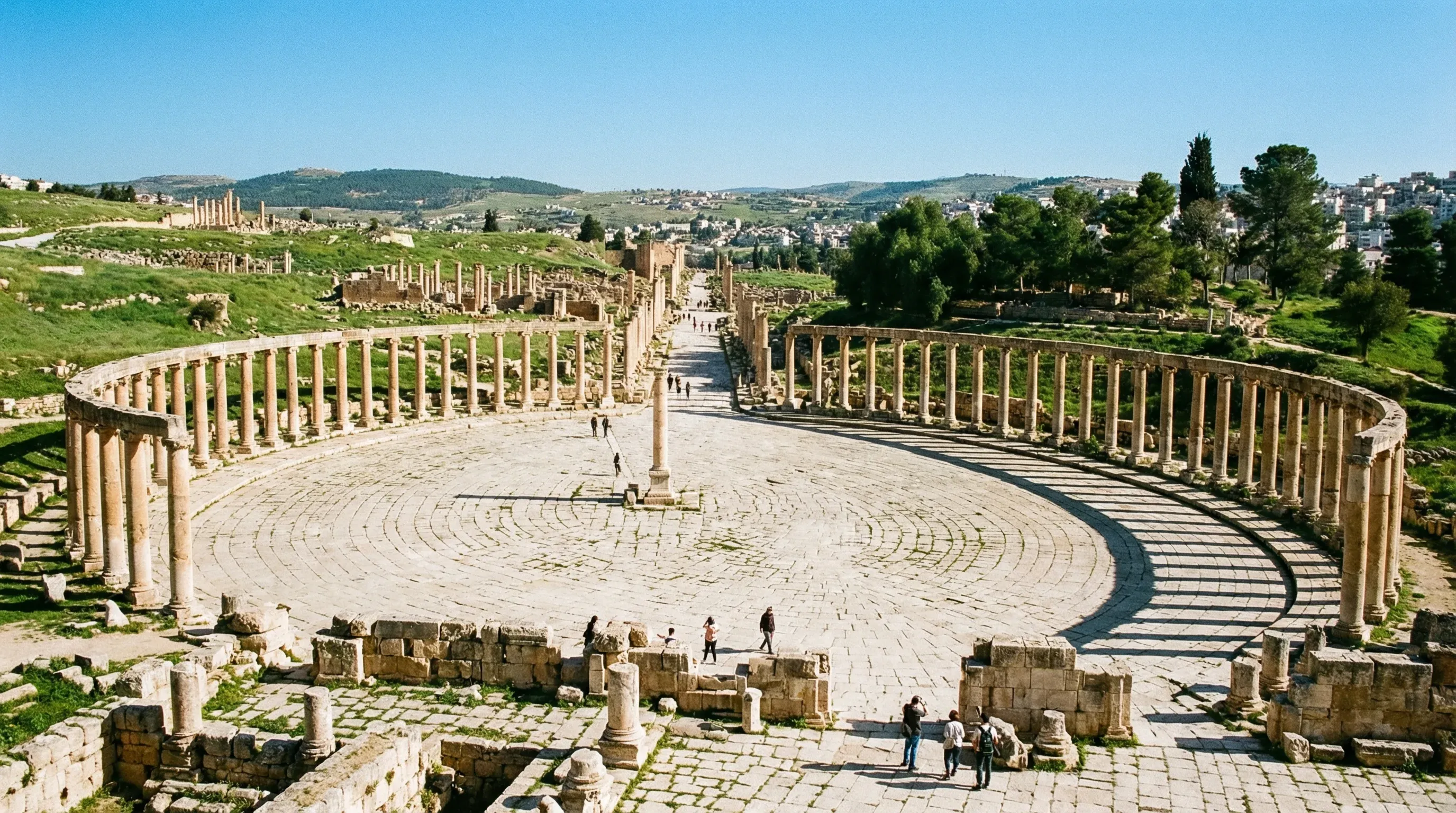 The large Oval Plaza in the ancient Roman city of Jerash, surrounded by a colonnade of Ionic stone pillars under bright sunlight.