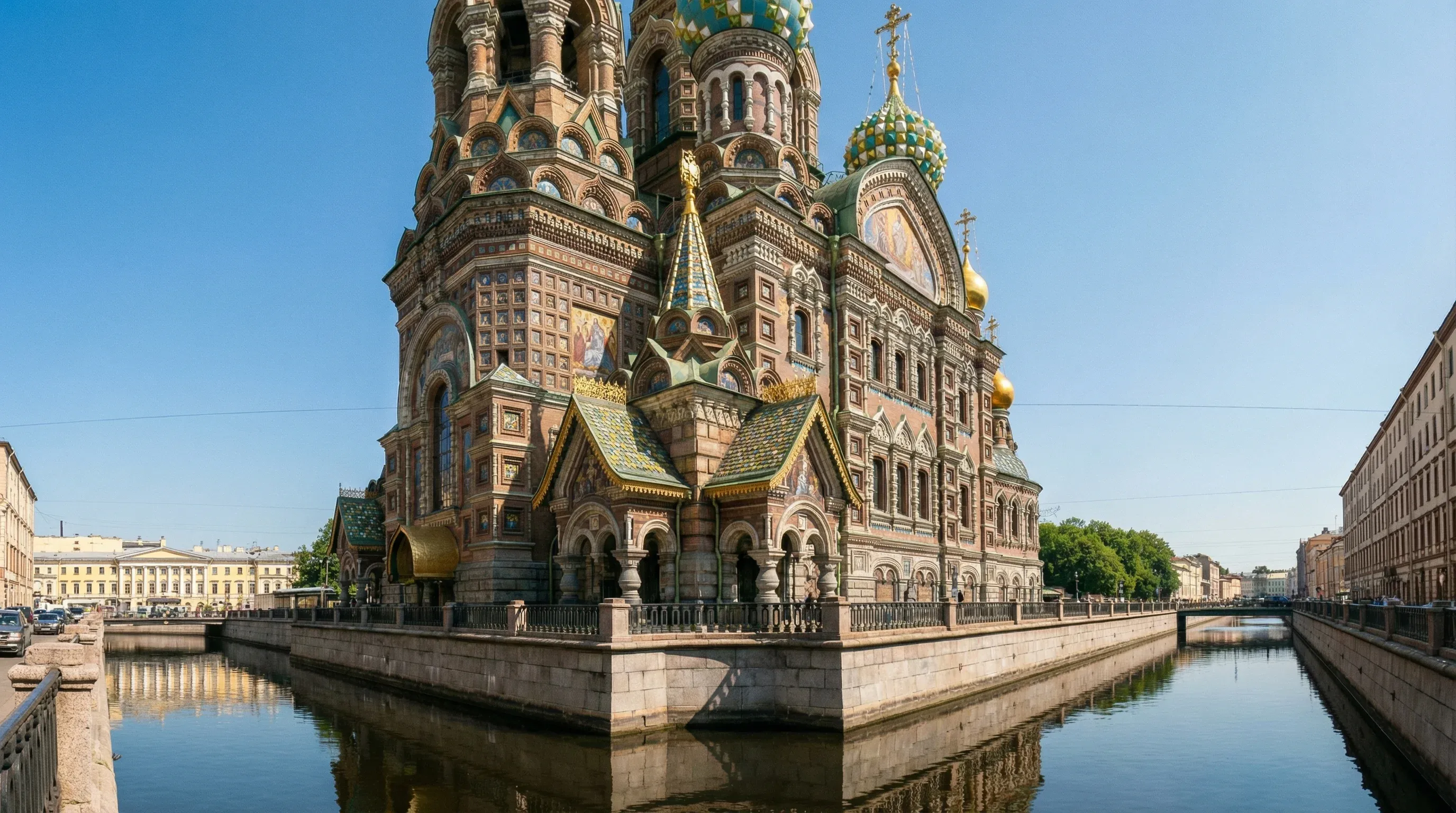 The Church of the Savior on Spilled Blood in Saint Petersburg viewed from the Griboyedov Canal under a clear sky.
