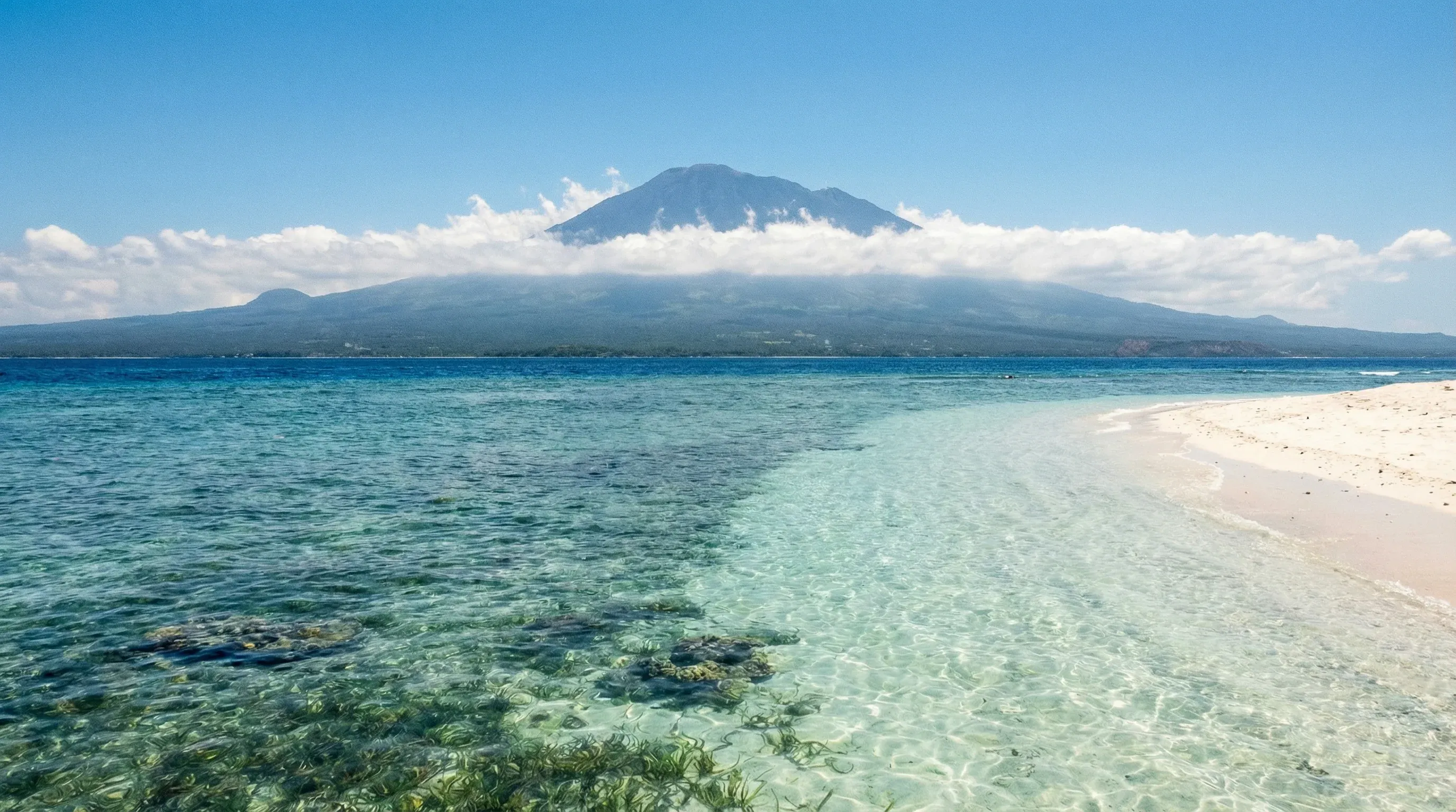 A white sand beach on Gili Trawangan with clear turquoise water and the silhouette of Mount Rinjani on the horizon.