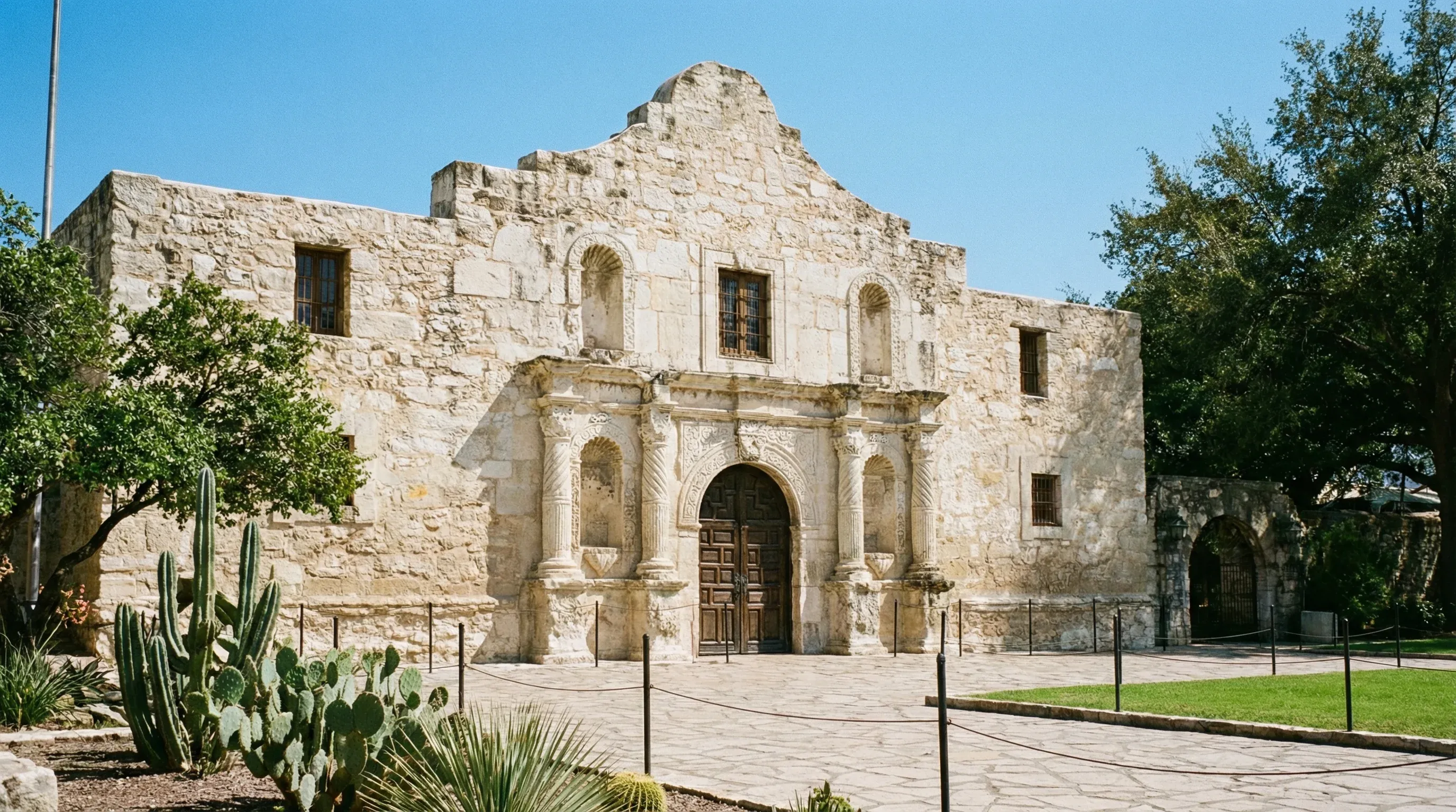 The historic stone facade of the Alamo mission building in San Antonio under a bright sun.