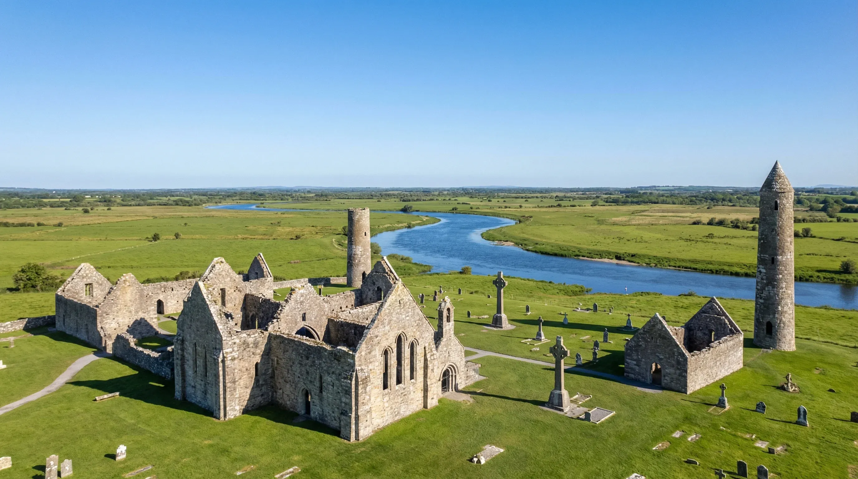 Ancient stone ruins including a round tower and cathedral at Clonmacnoise, located on the grassy banks of the River Shannon.